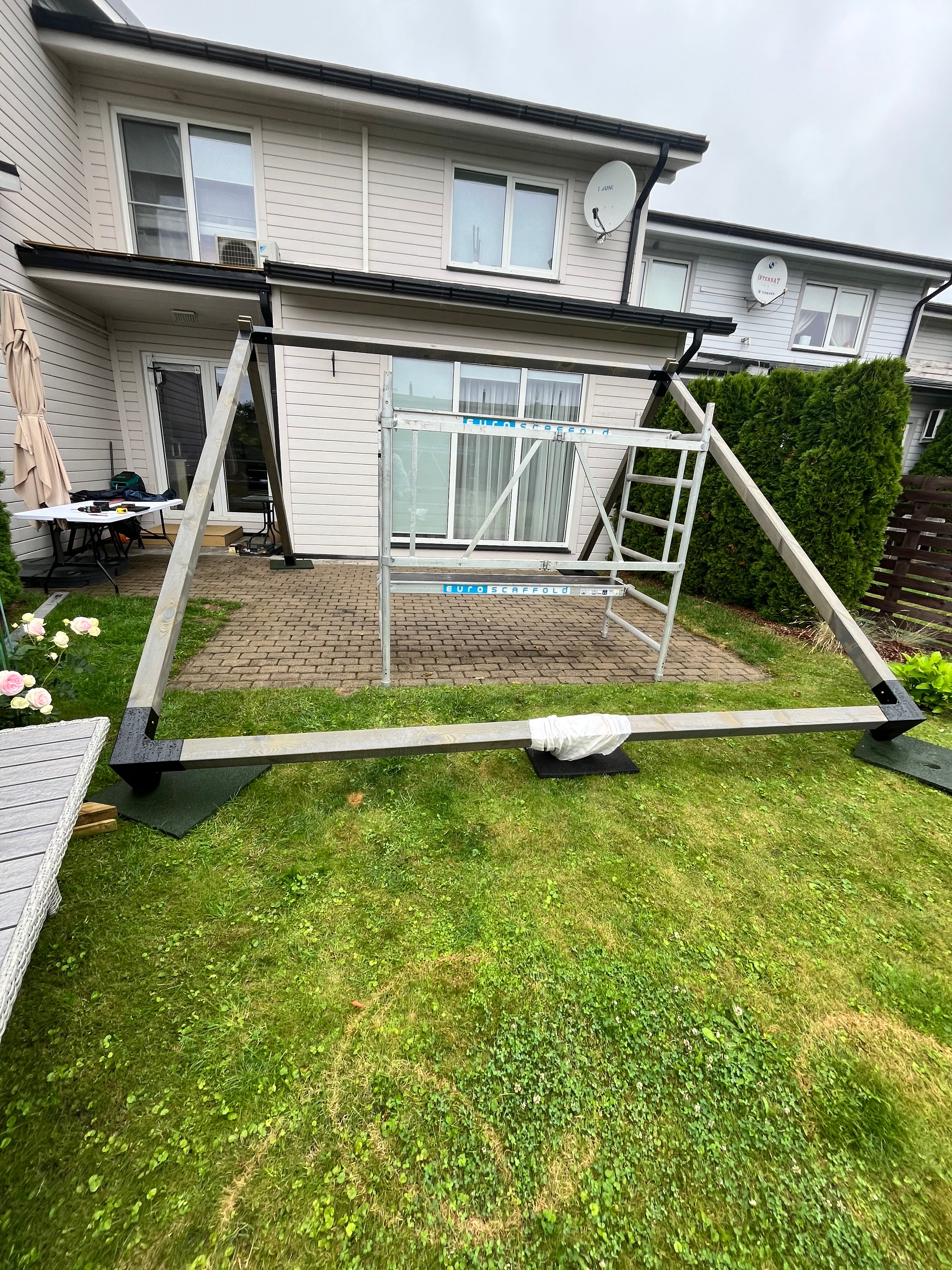 Outdoor patio area with a pergola attached to a house, featuring grass and a small garden.