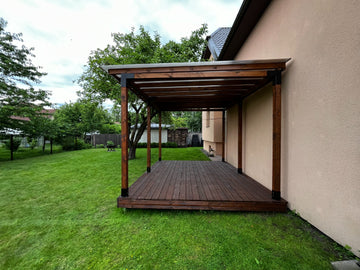 Wooden pergola next to a house with green grass and trees in the background