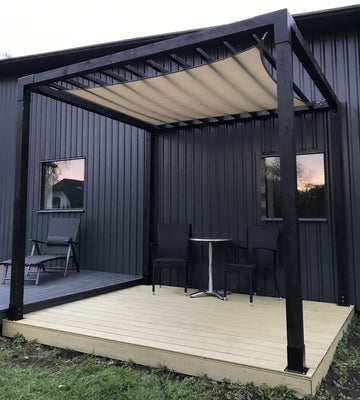 Outdoor patio with pergola, table, and chairs against a dark gray building.