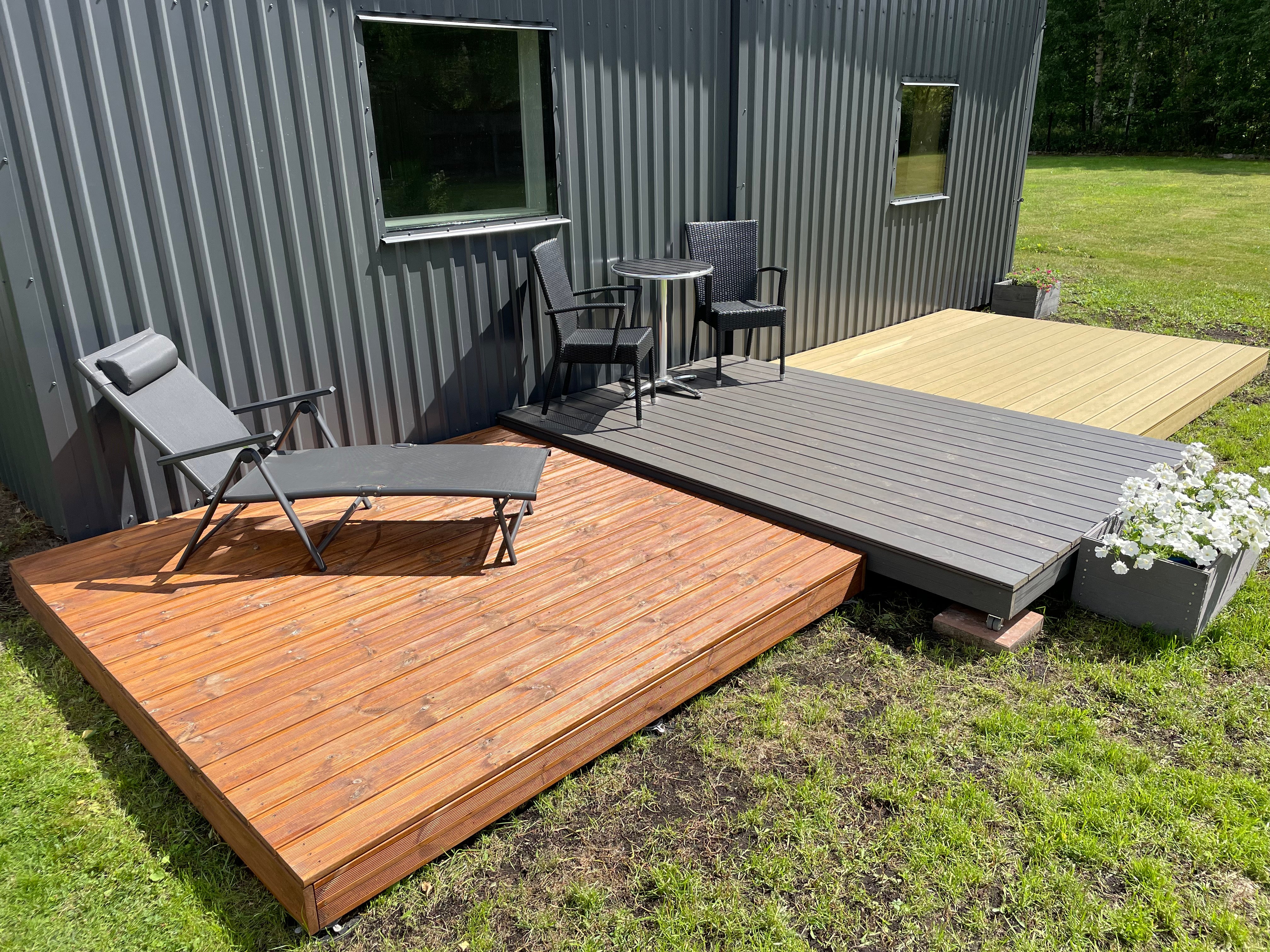 Two wooden decks with outdoor furniture in front of a modern building.