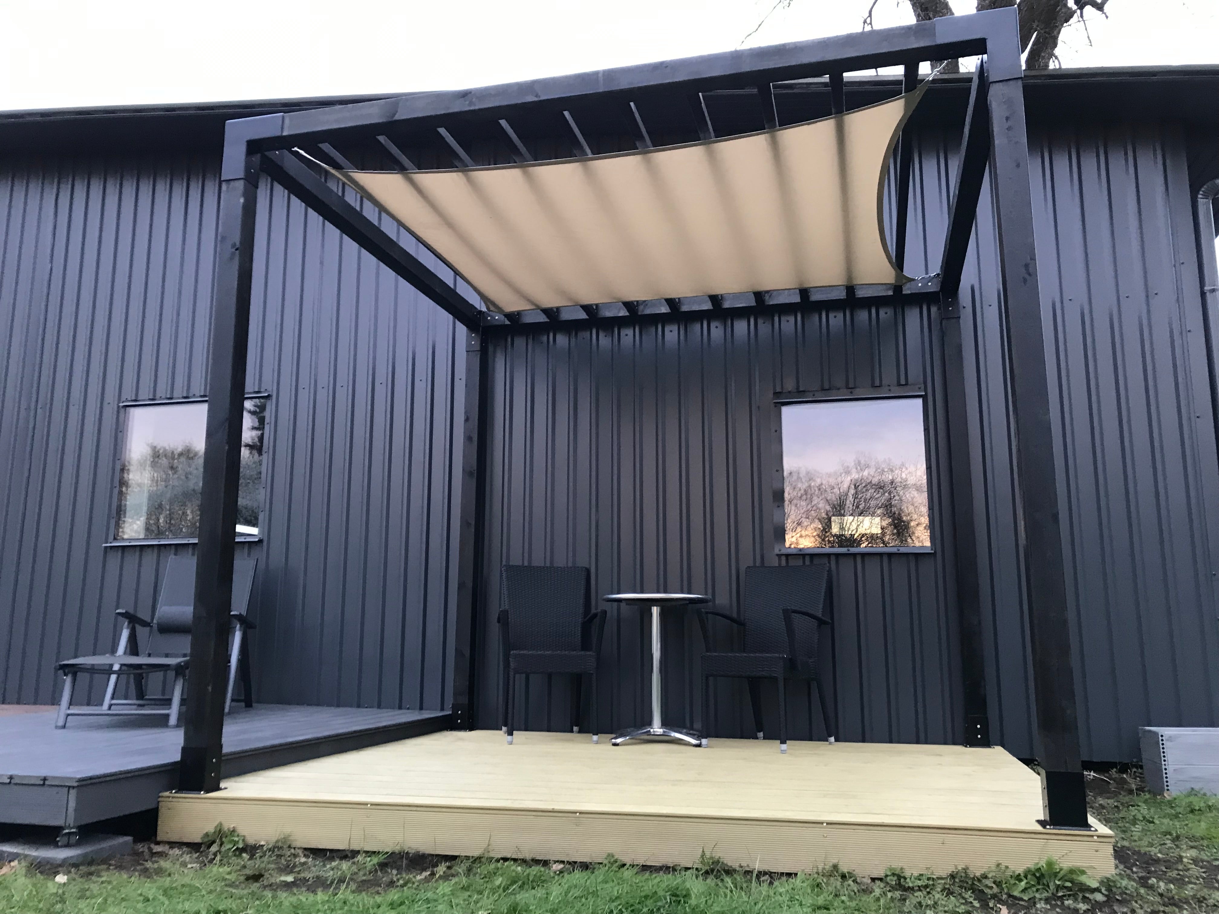 Outdoor patio area with a black pergola and furniture against a gray building.