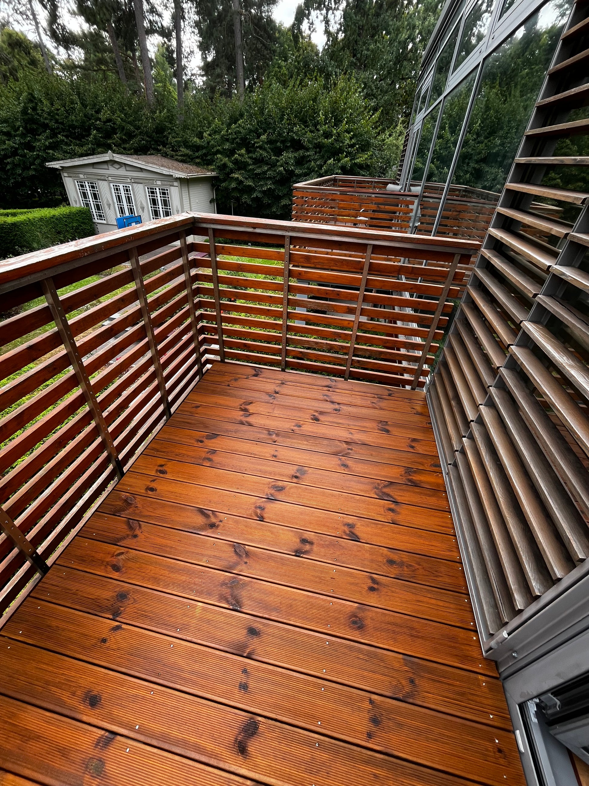 Wooden deck with a railing and view of trees and a house in the background