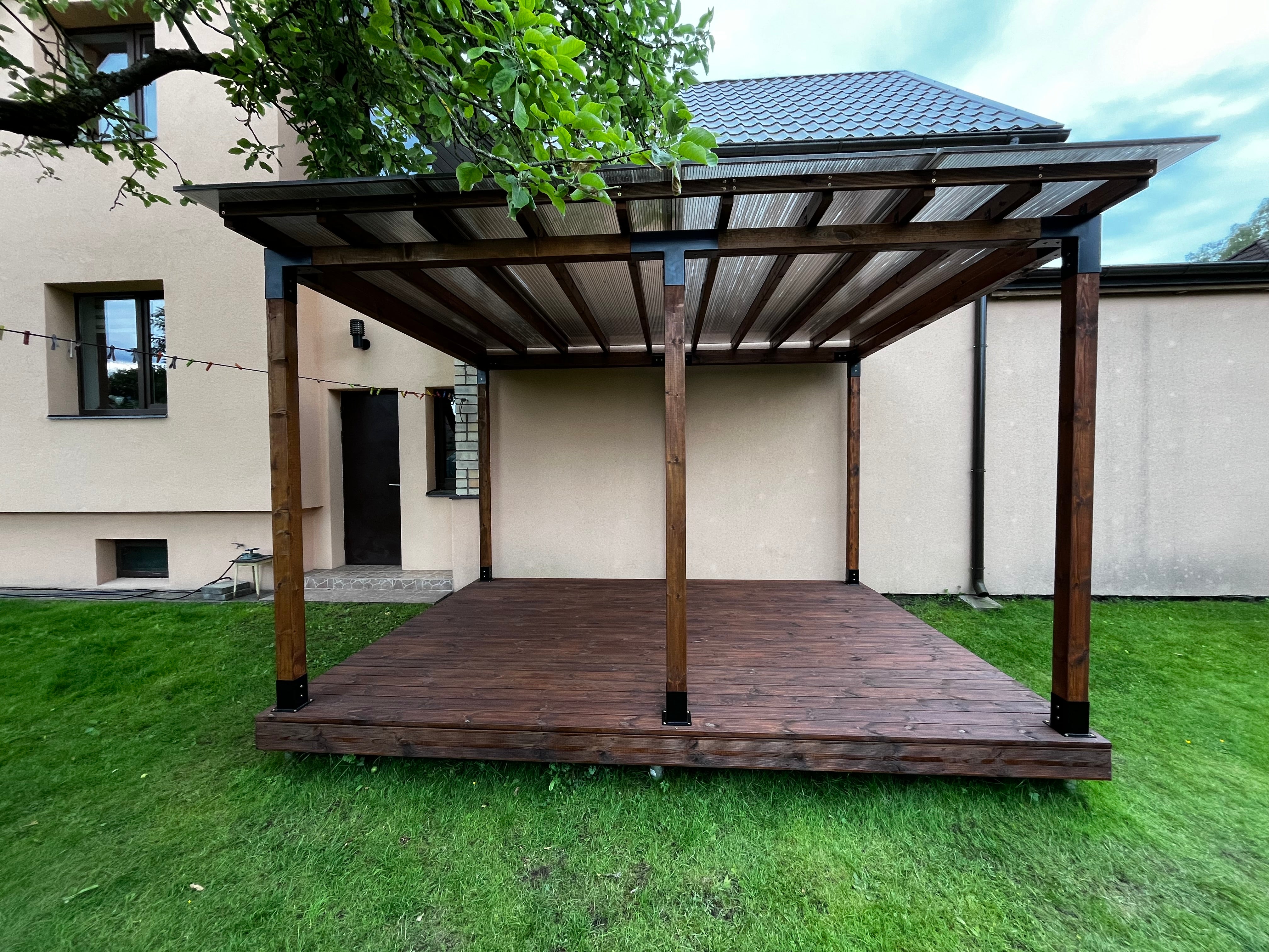 Wooden pergola structure on a grassy area with a building in the background