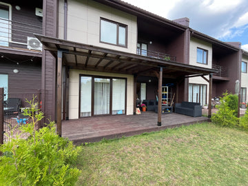 Two-story house with a large deck, canopy and outdoor furniture on a sunny day.
