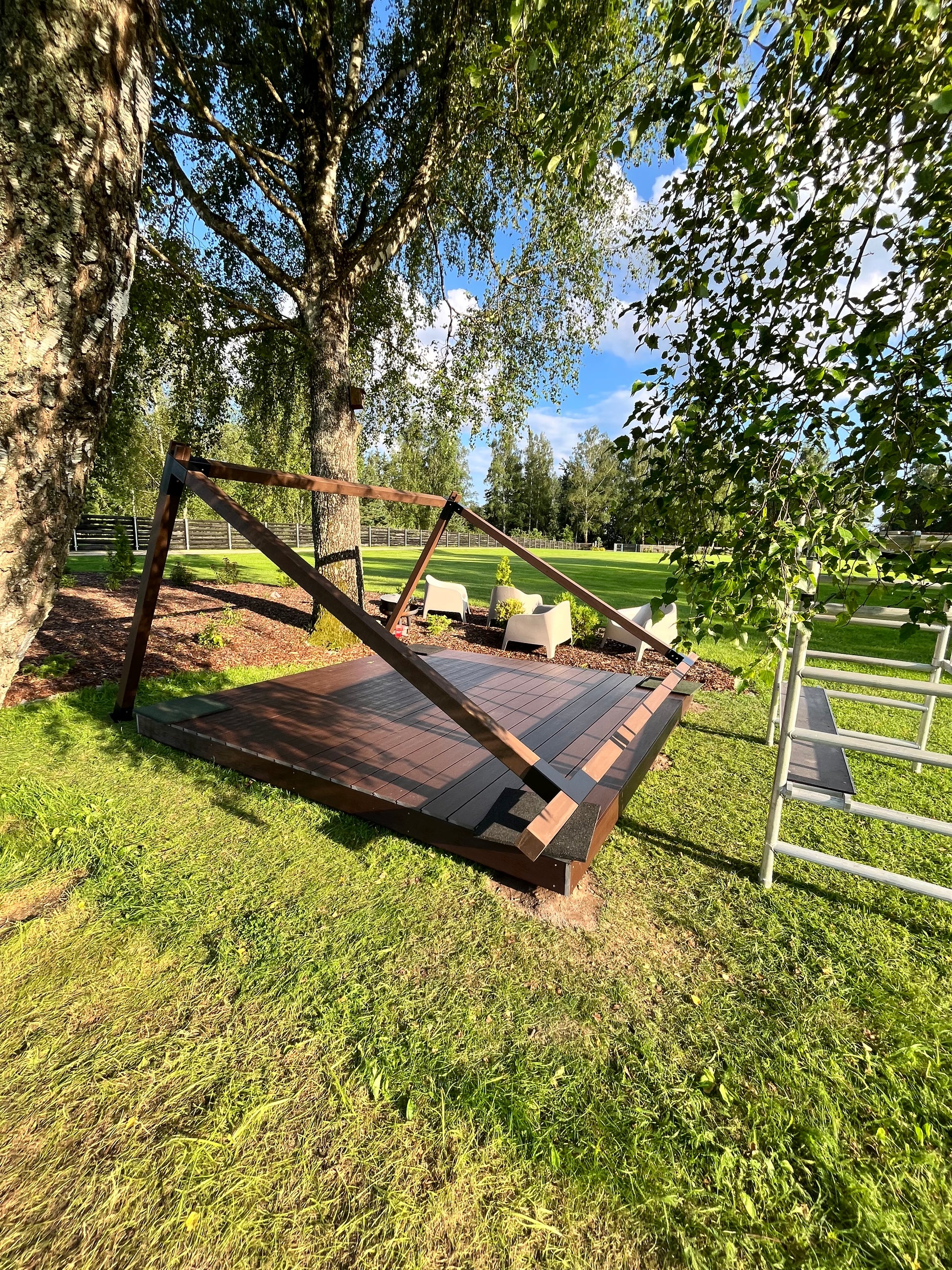 Wooden swing set on grass with trees and sky in the background