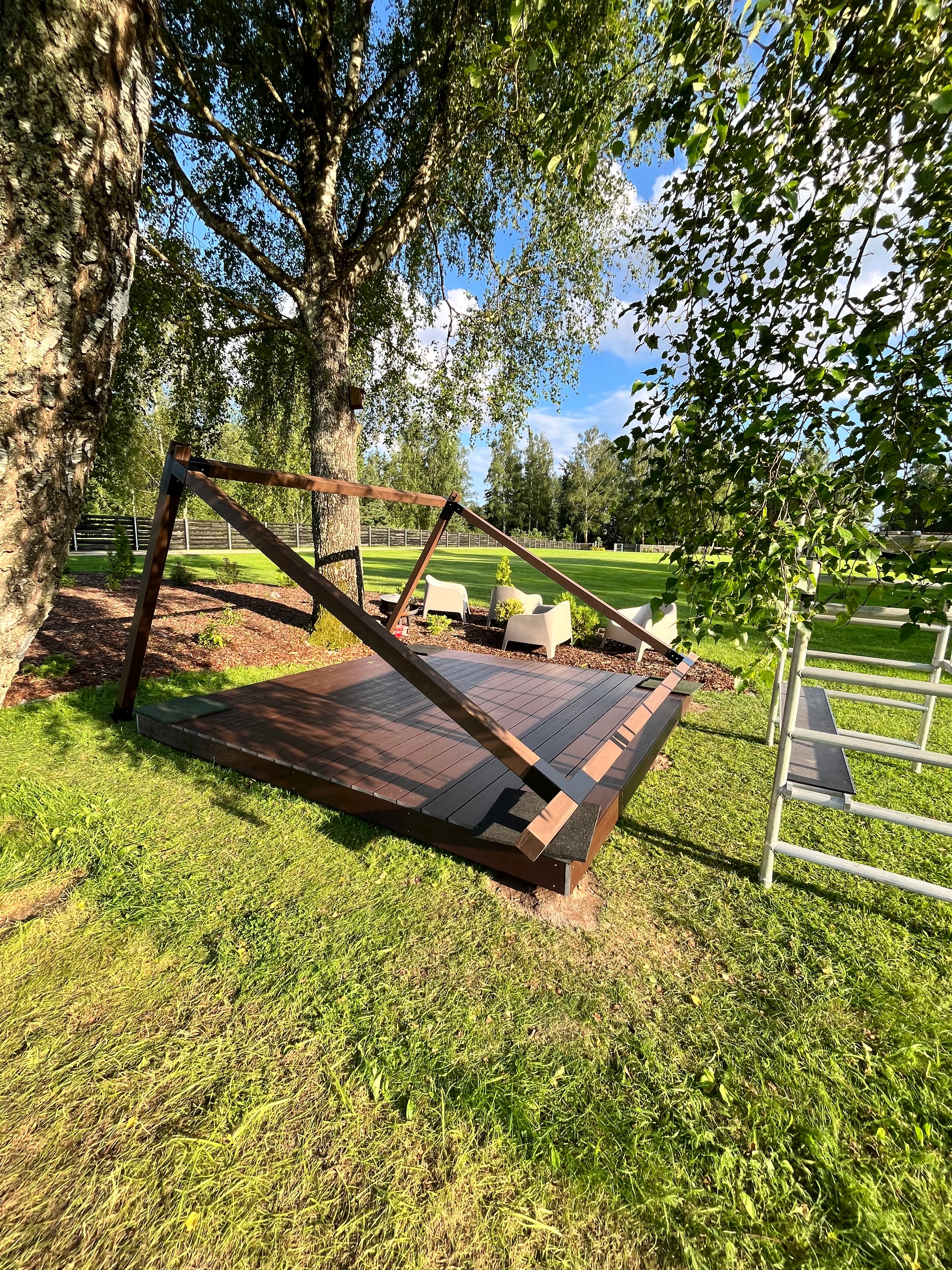 Wooden swing set on grass with trees and sky in the background