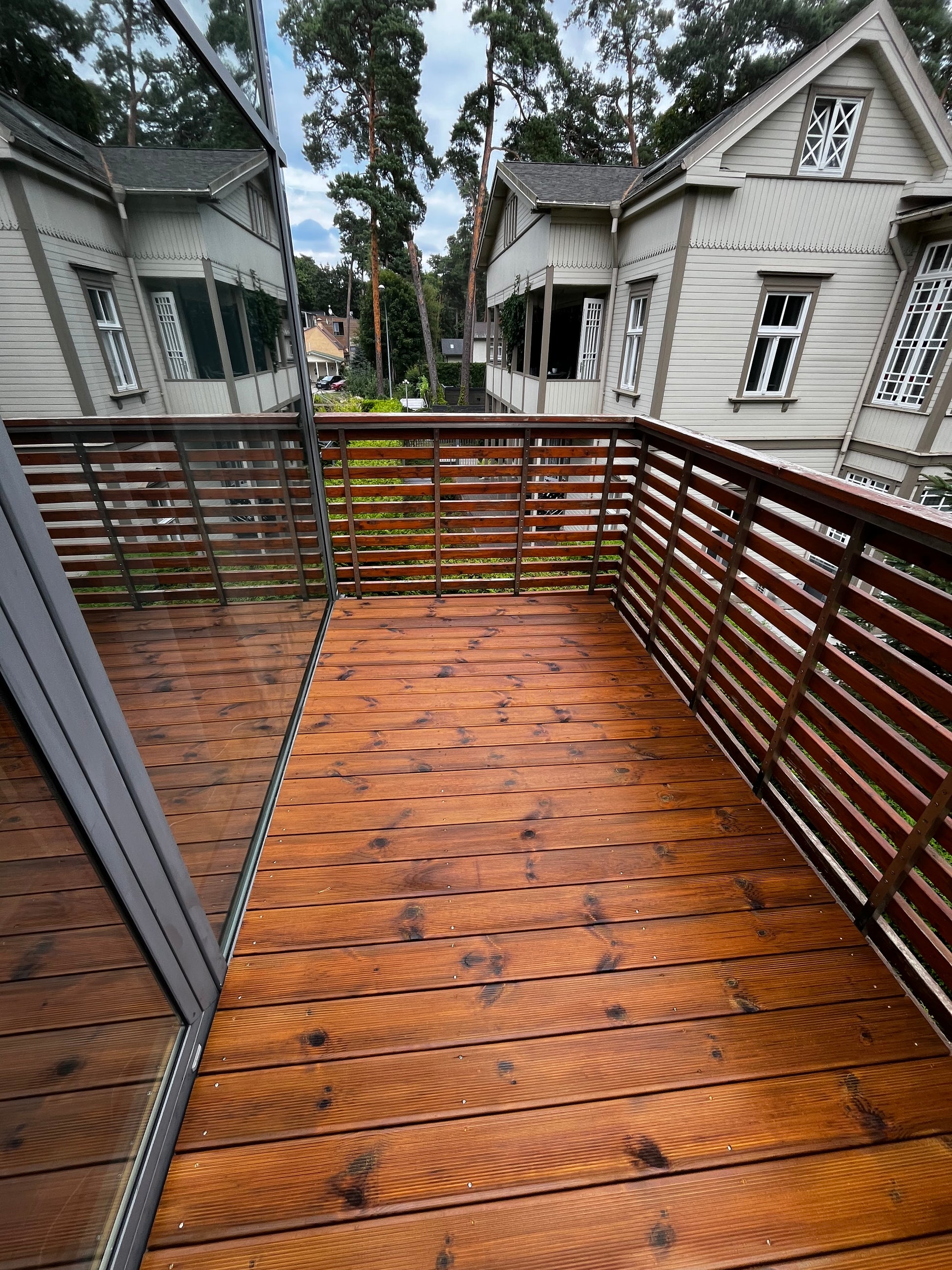 Wooden deck with railing overlooking a house and trees