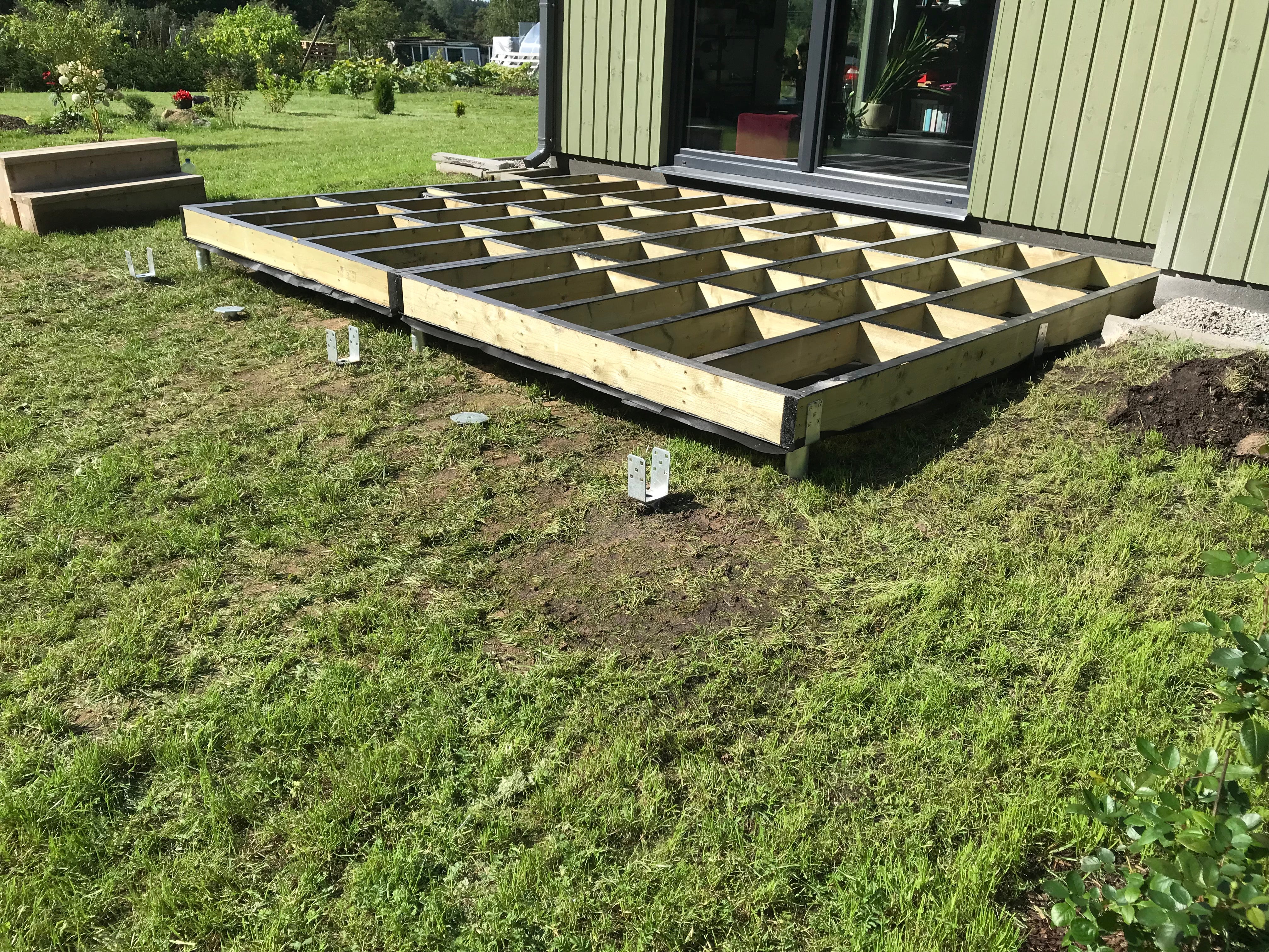 Wooden deck foundation on a grassy area with a house in the background