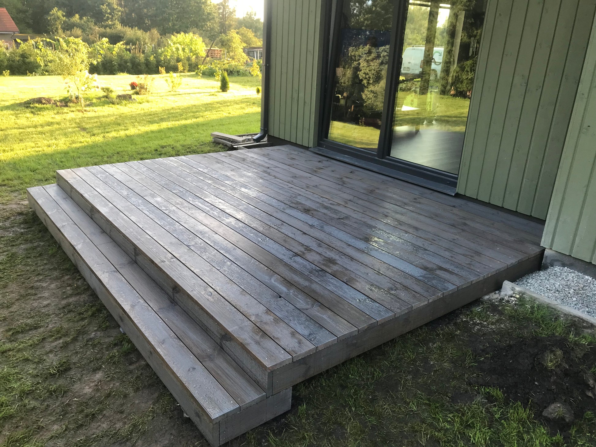 Wooden deck with steps leading up to a house with large windows.