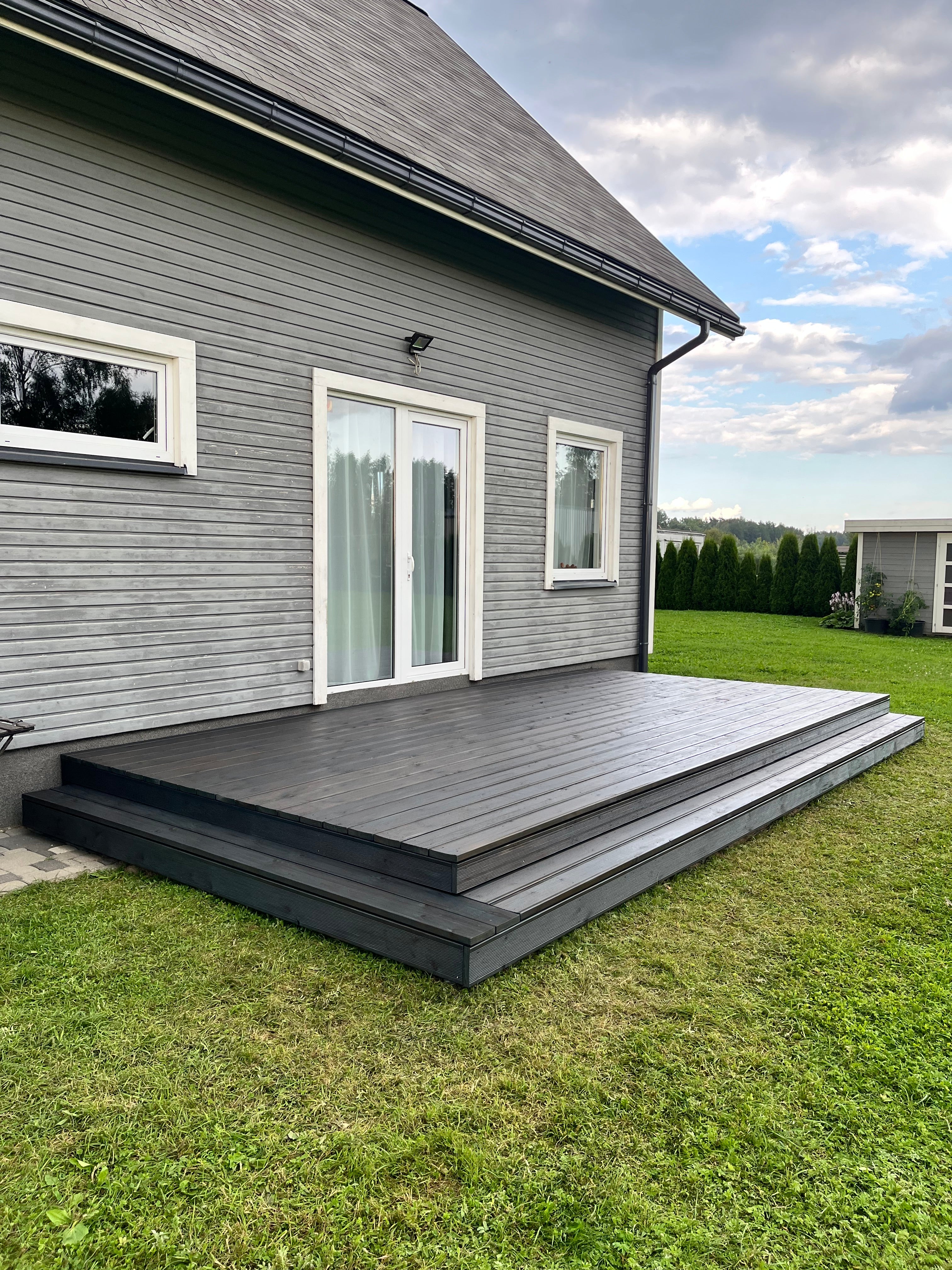 House exterior with gray siding and white windows on a grassy lawn.