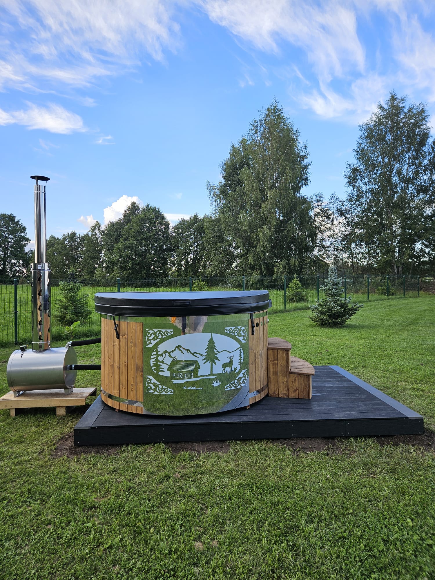 Wood-fired hot tub with sauna house design on a grassy area with trees in the background