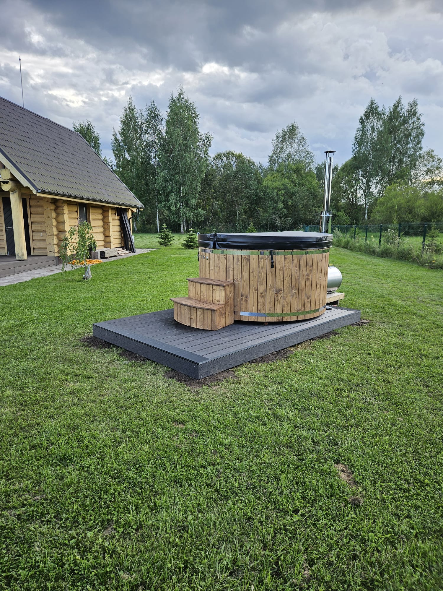 Wooden hot tub on a grassy area with a cabin in the background