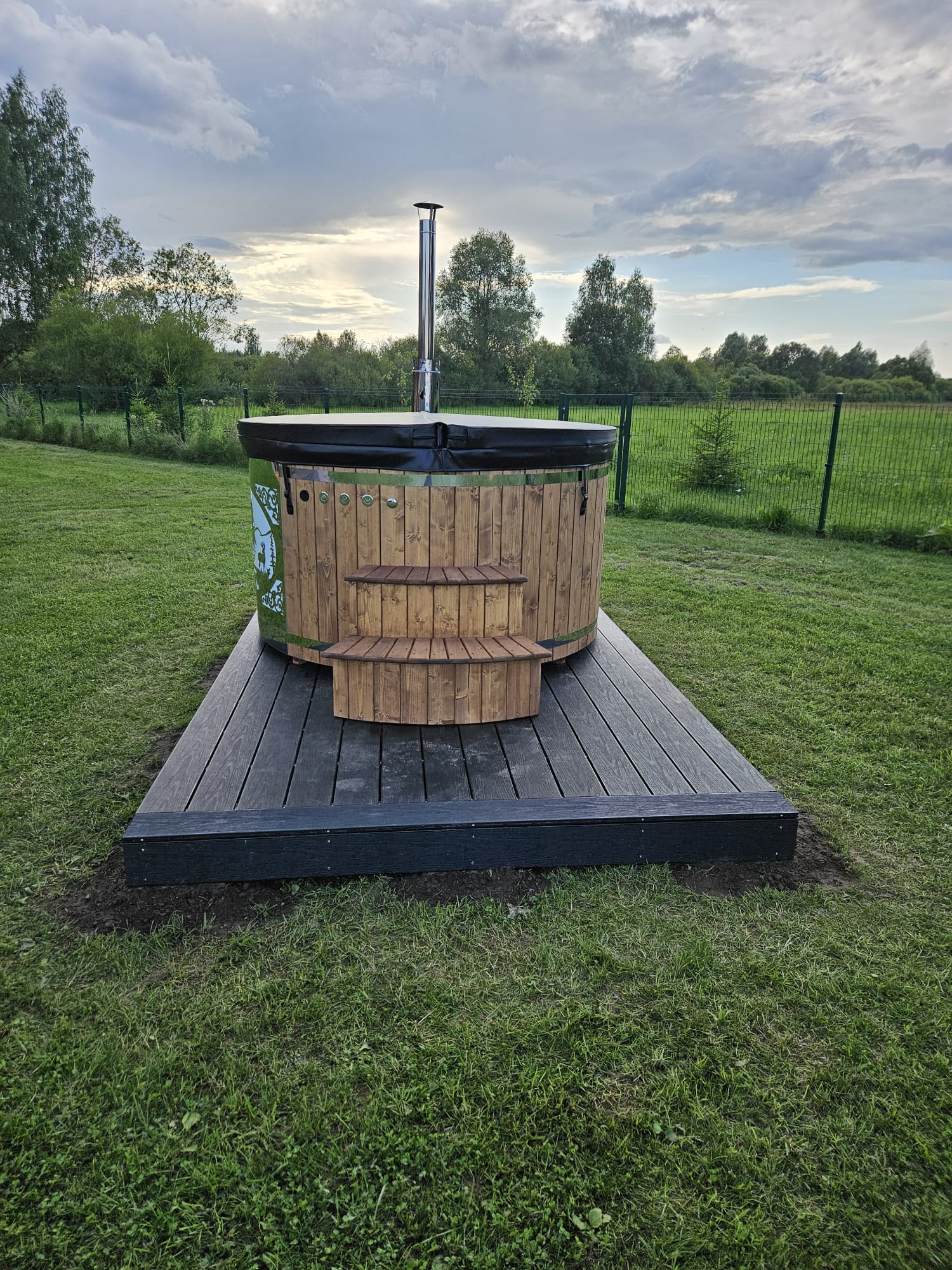 Wooden hot tub on a platform in a grassy outdoor area with trees in the background