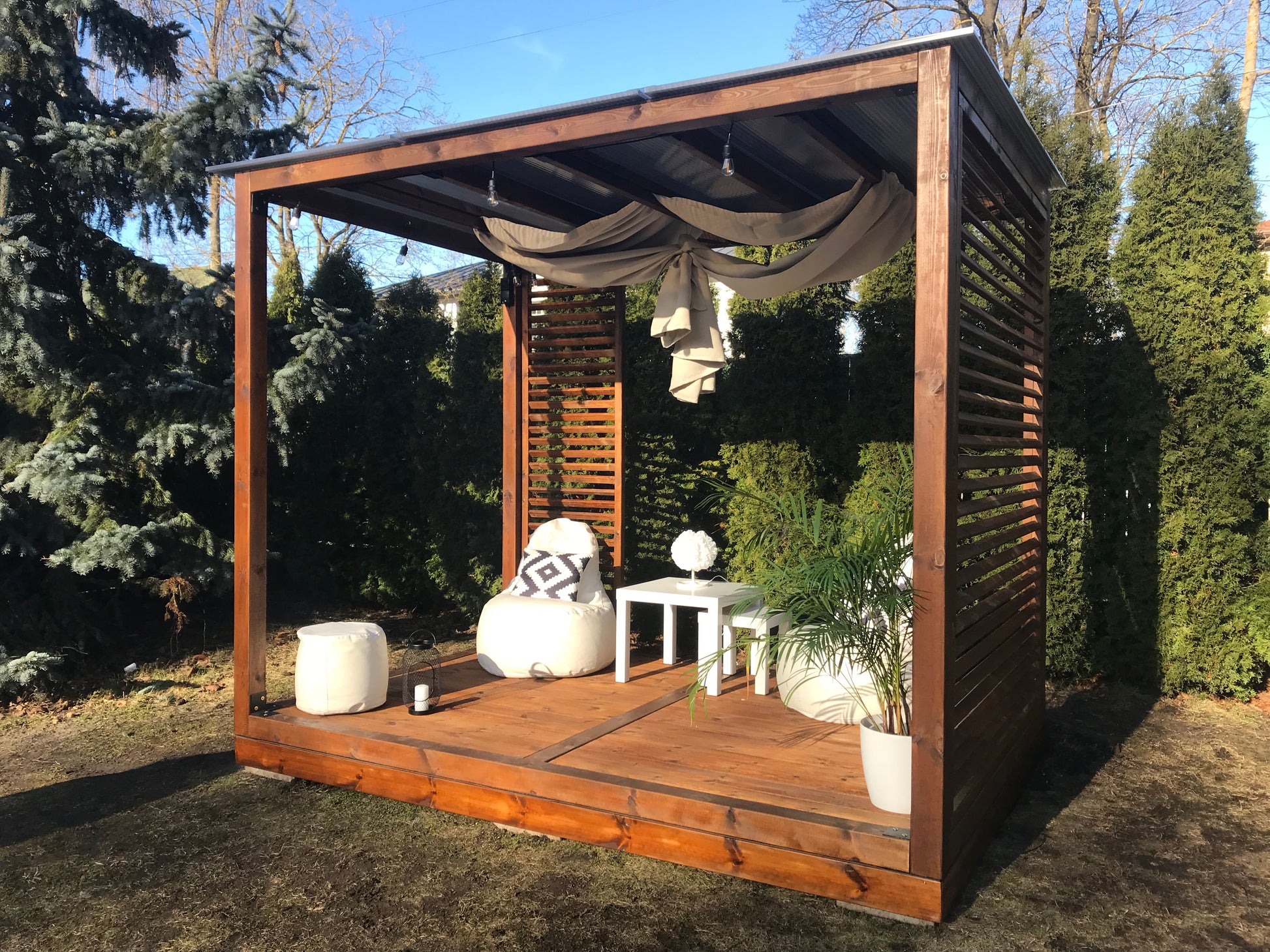 Wooden outdoor gazebo with furniture and decor in a garden setting