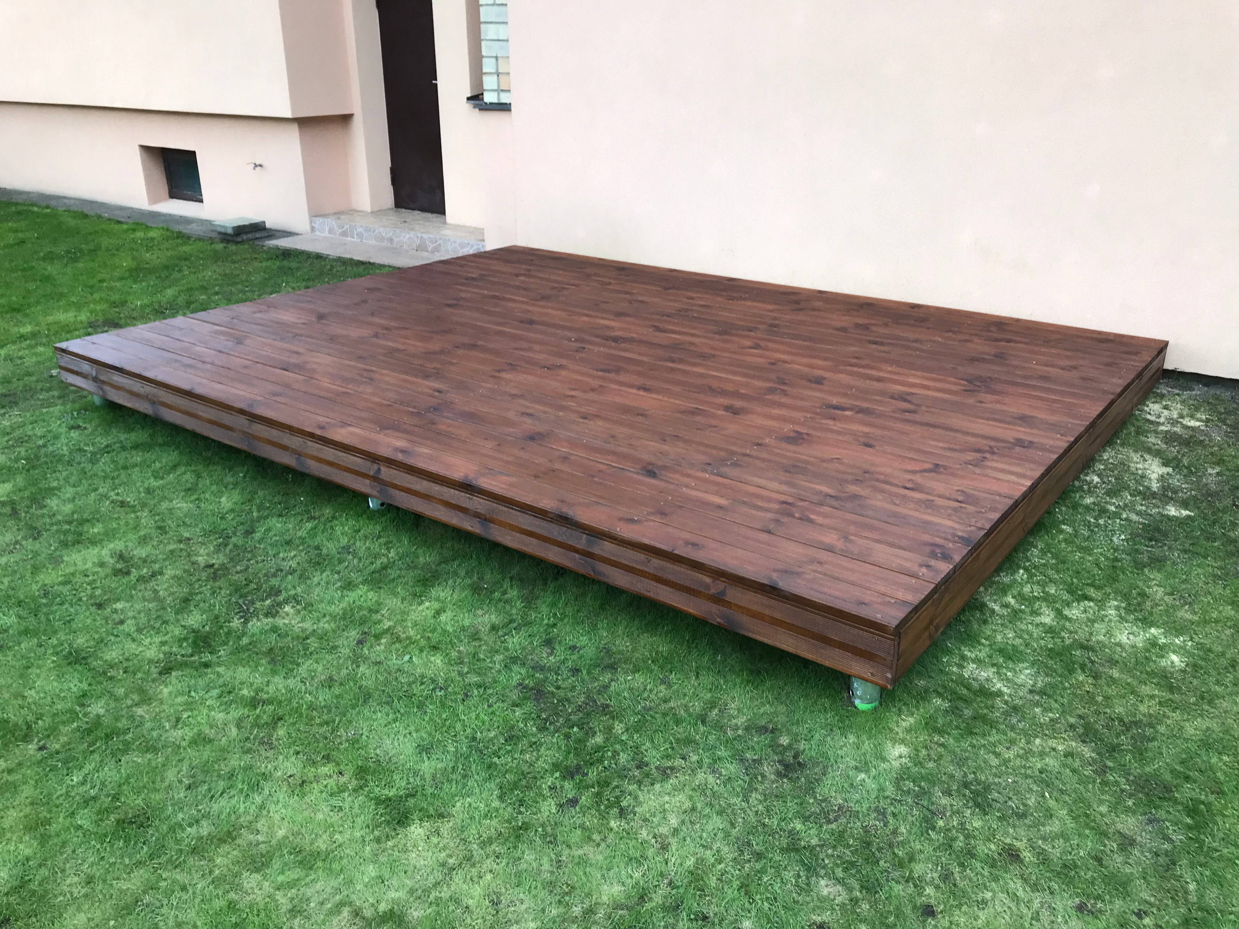 Wooden deck on grass with a building in the background
