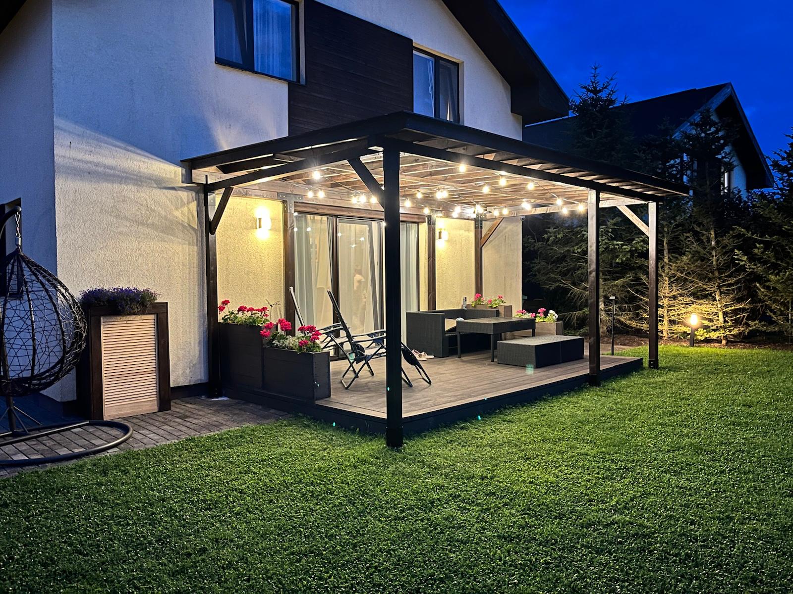 Outdoor patio area with a covered deck, chairs, and plants at night.