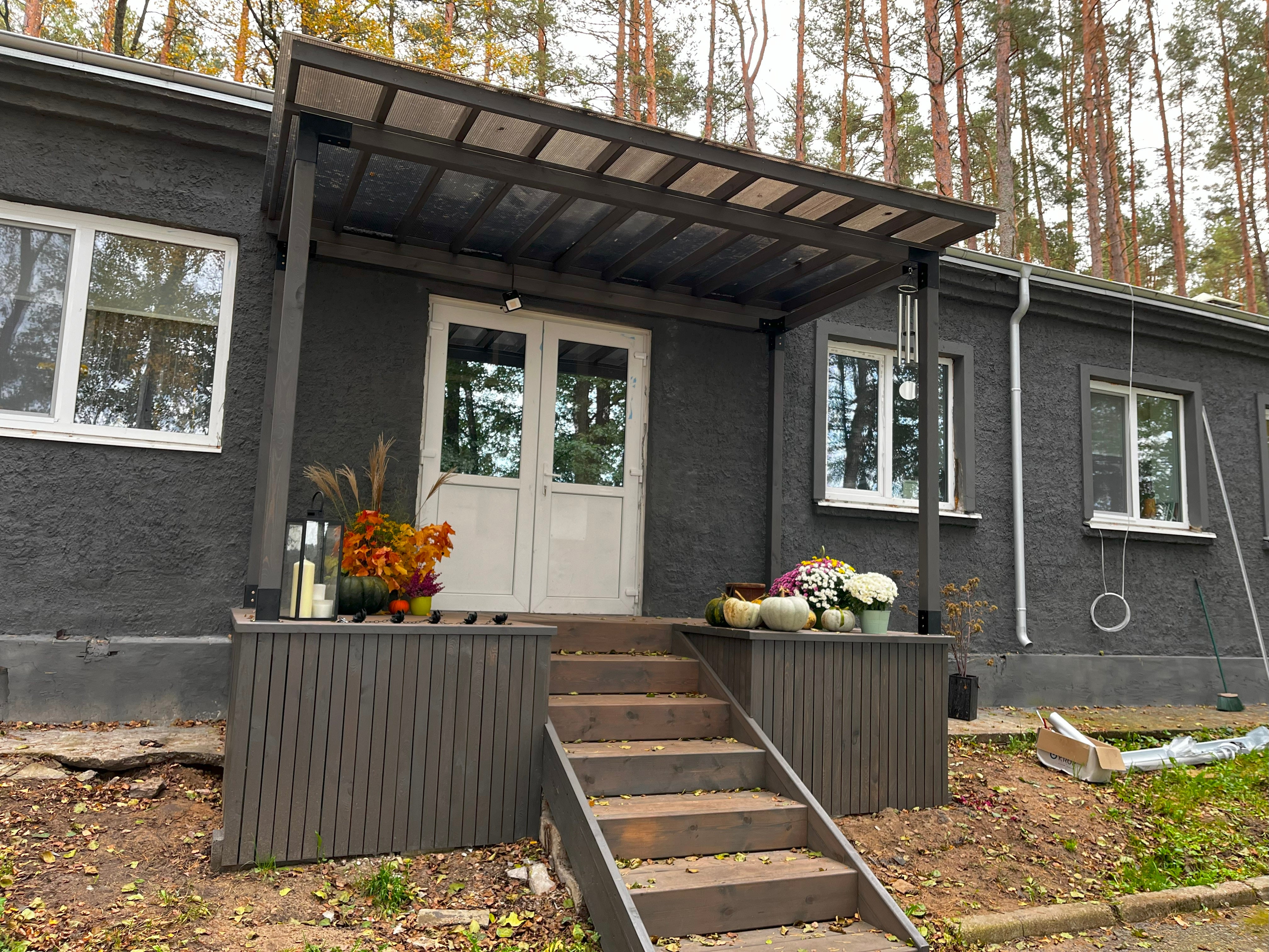 Gray house with a wooden deck and steps leading up to it, surrounded by trees.