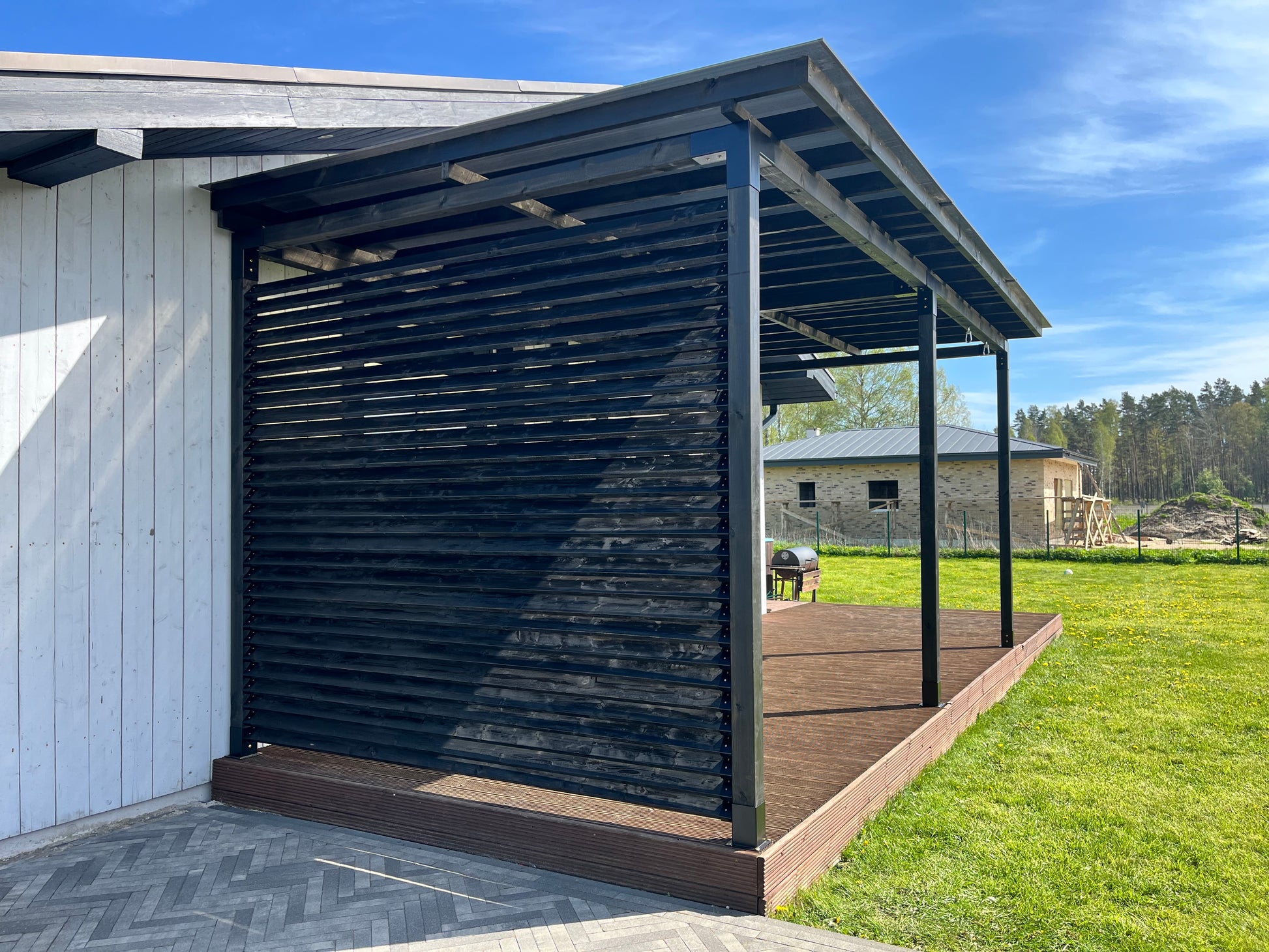 Modern outdoor structure with a metal roof and wooden deck, set against a blue sky.