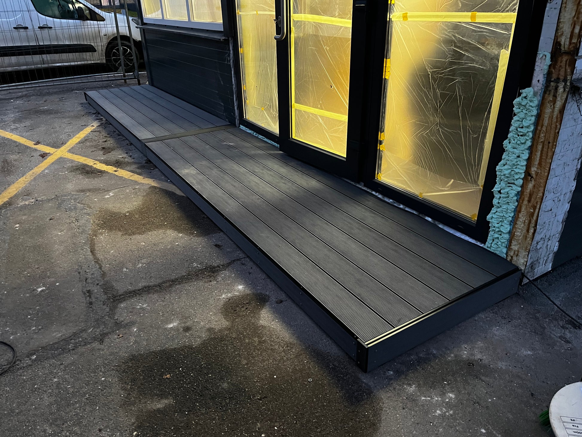 Wooden ramp leading up to a glass door with yellow lines on the pavement.