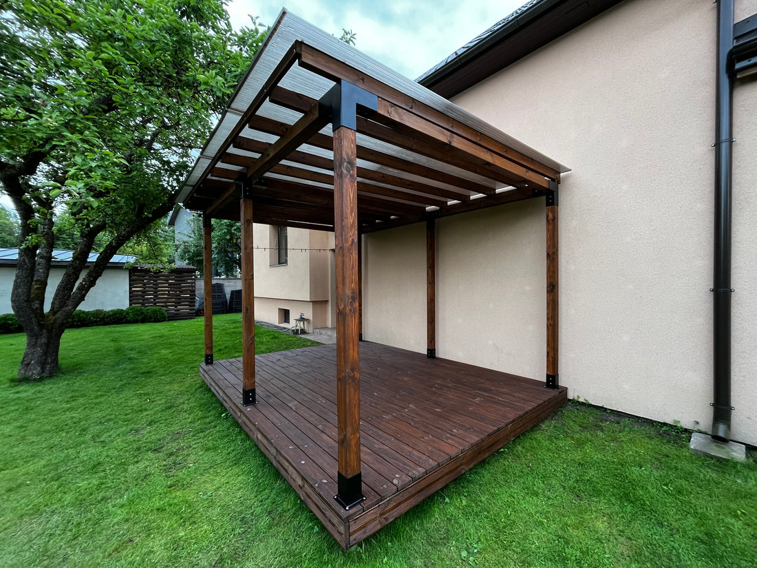 Wooden pergola attached to a house with green grass and trees in the background
