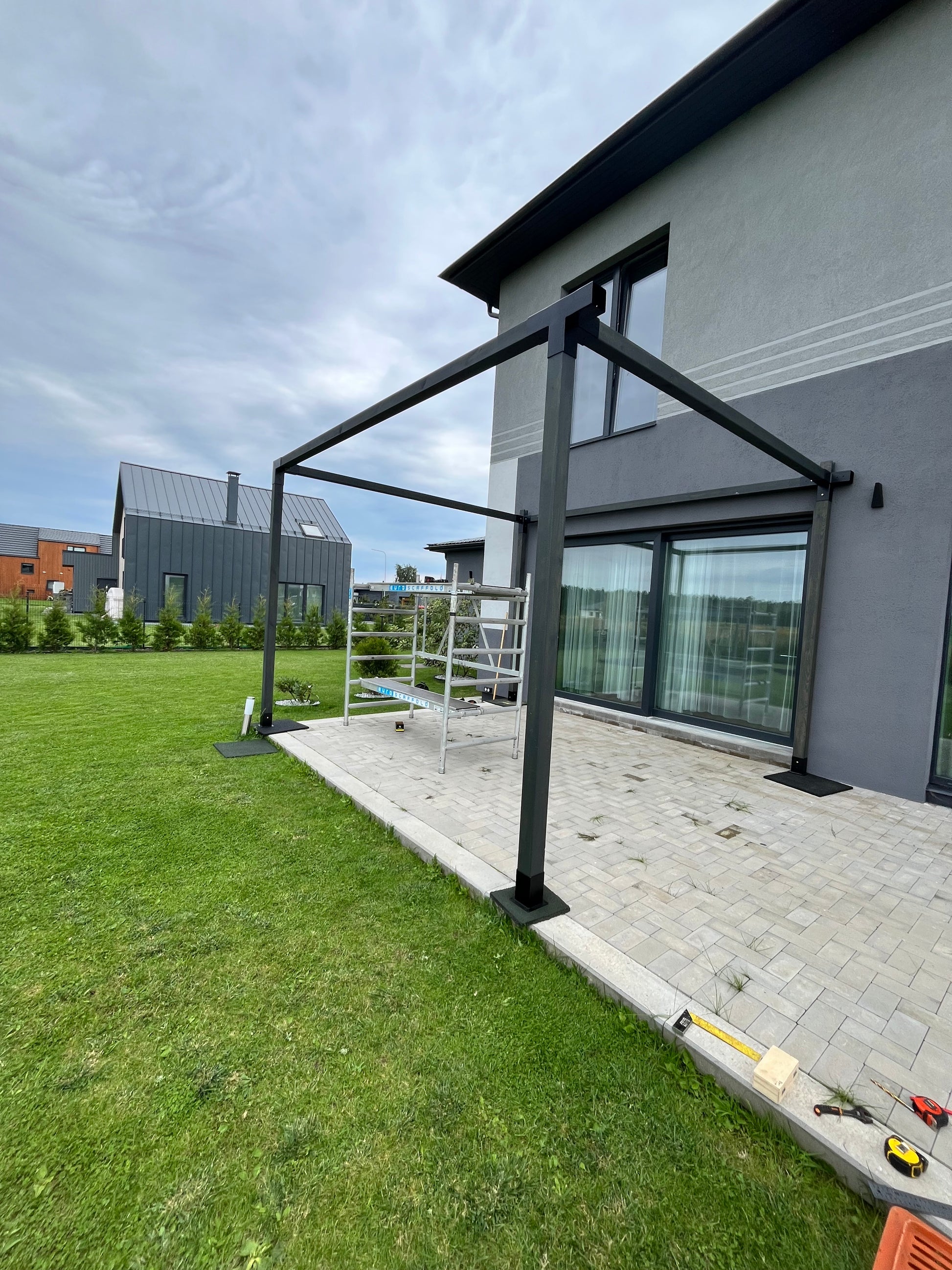 Black metal pergola structure on a grassy area with a modern house in the background
