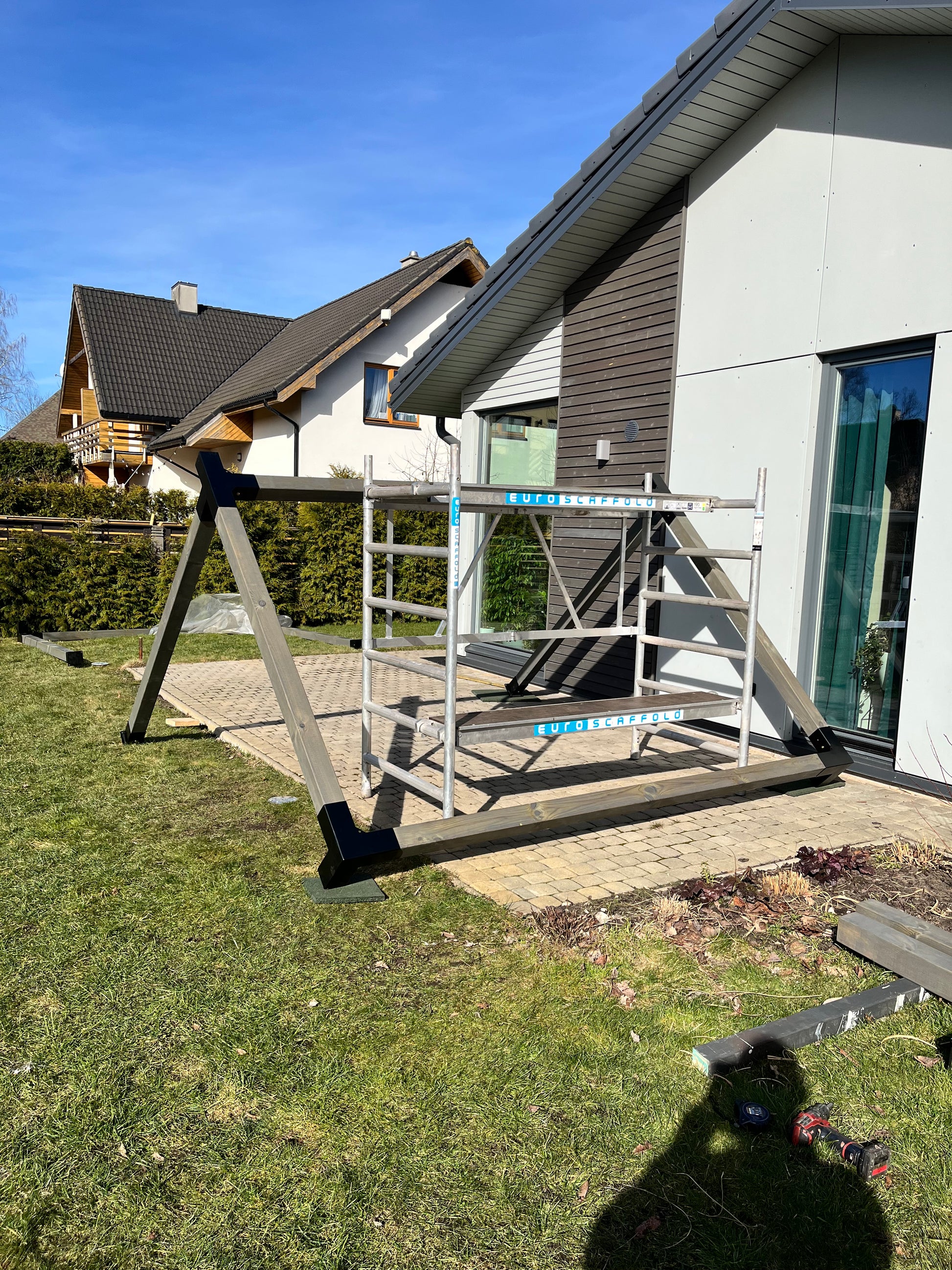Patio area with a wooden deck and grassy lawn in front of a modern house.