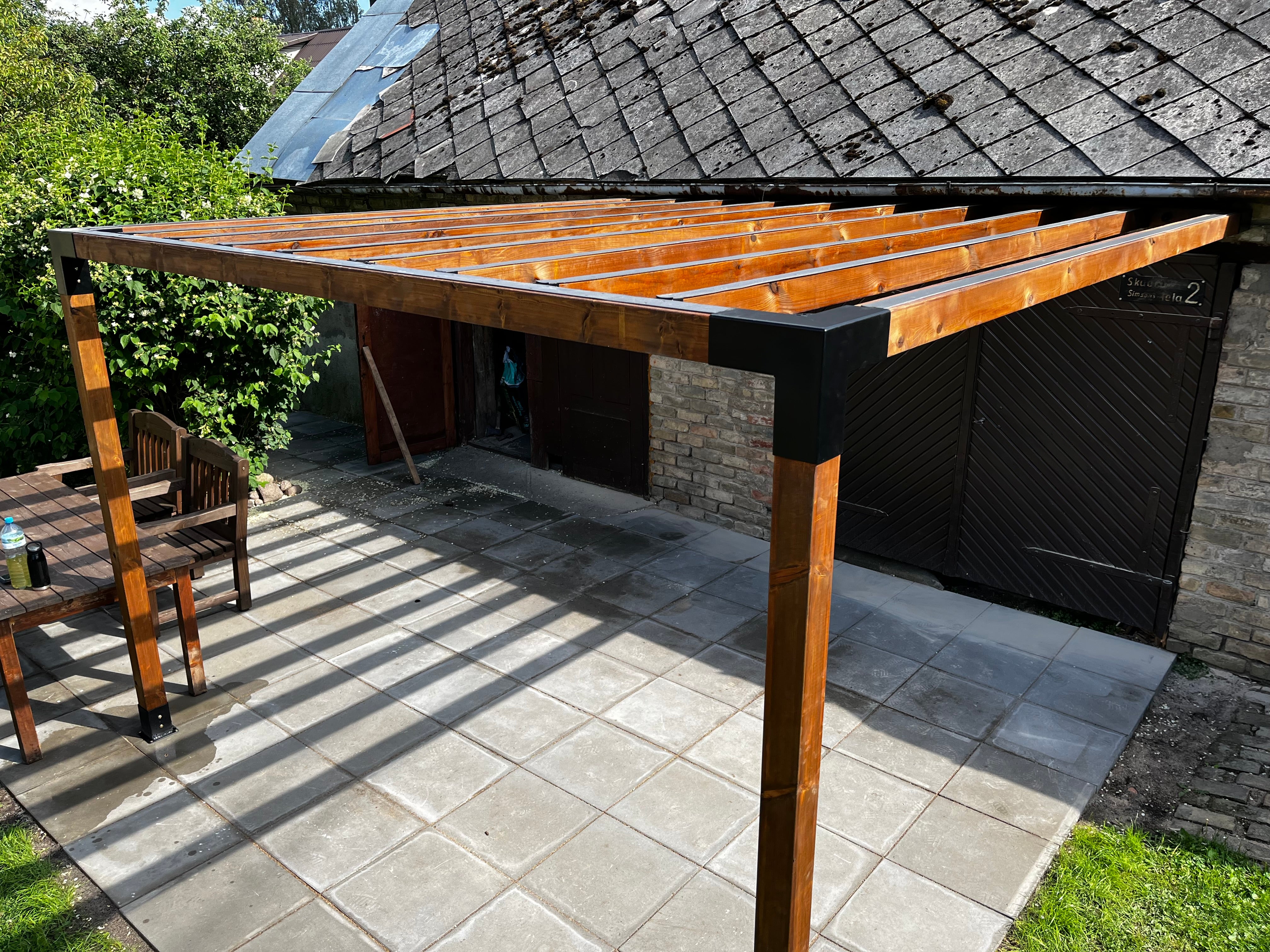 Wooden pergolaattached to a house with outdoor furniture underneath