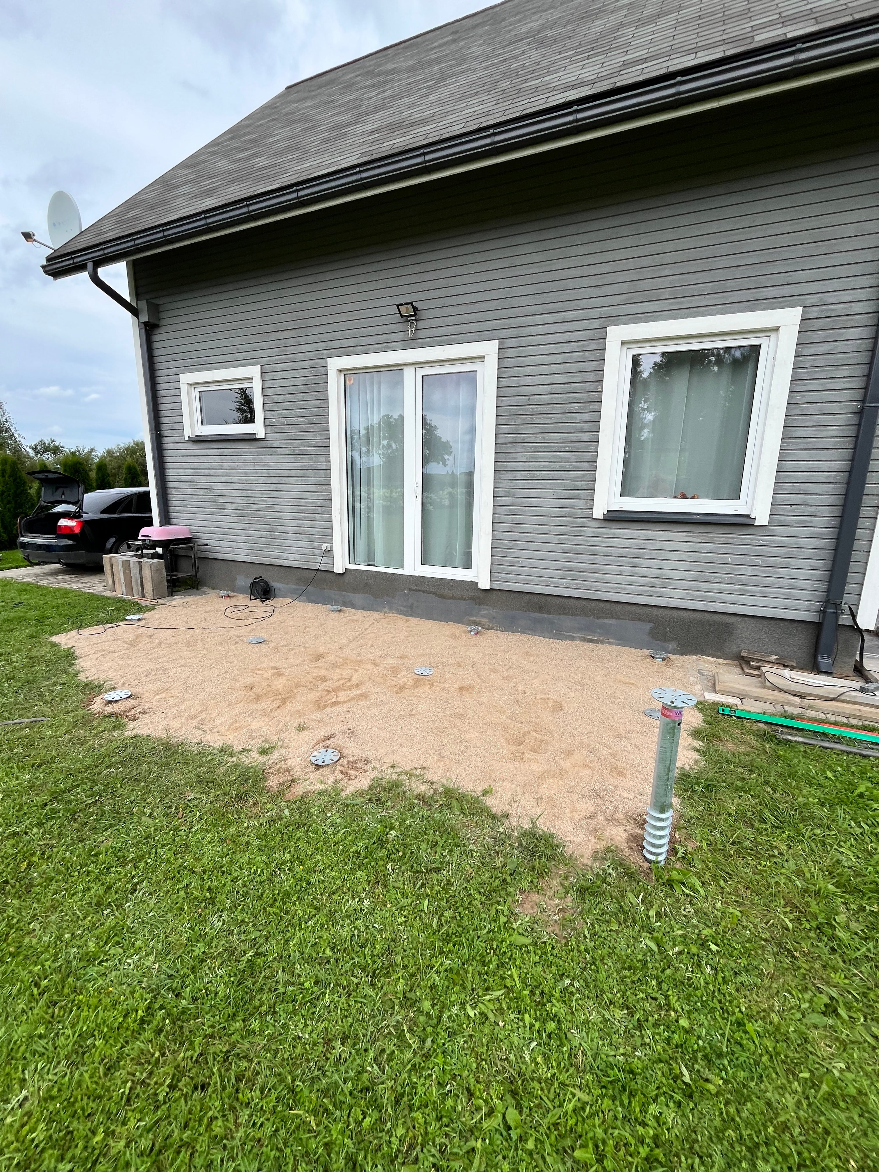 Gray house with white windows and a patch of dirt in front, with grass on the right side.