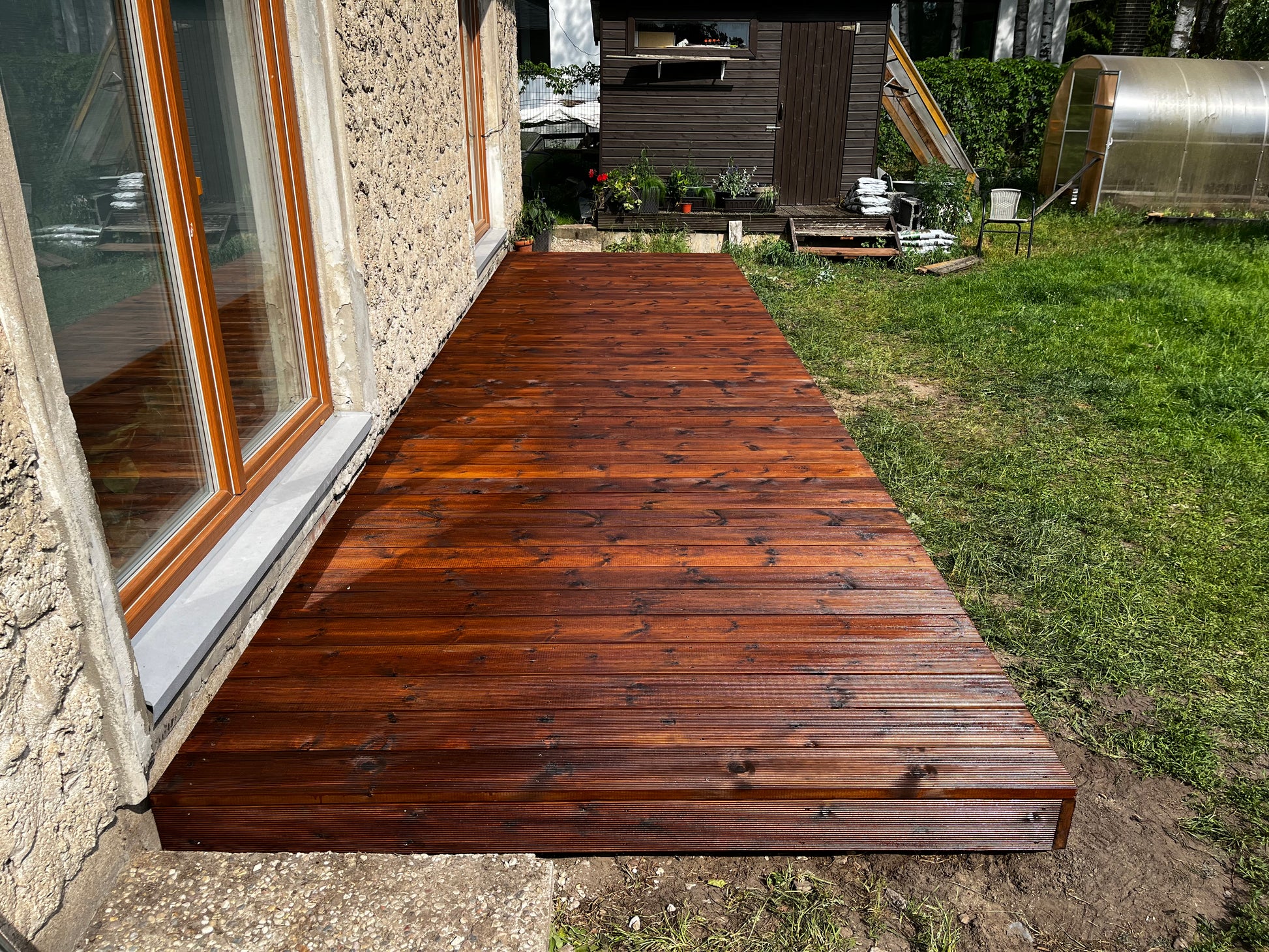 Wooden deck extending from a building with a grassy area and garden in the background