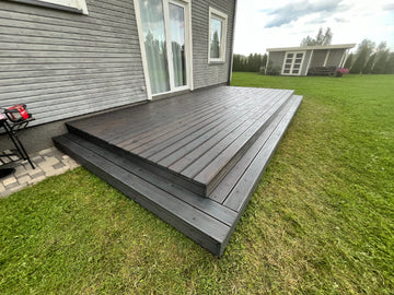 Wooden deck extending from a house with grassy area and another house in the background