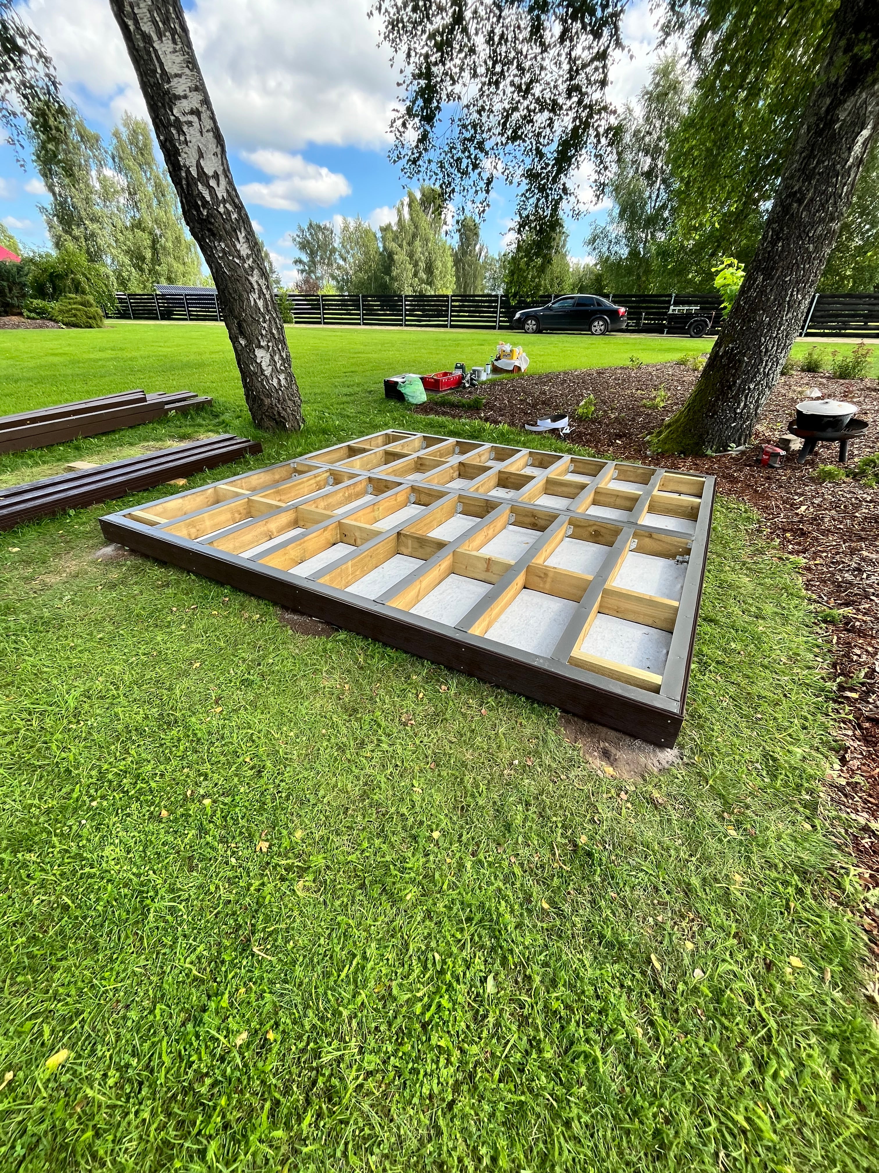 Wooden deck frame on grass with trees and sky in the background