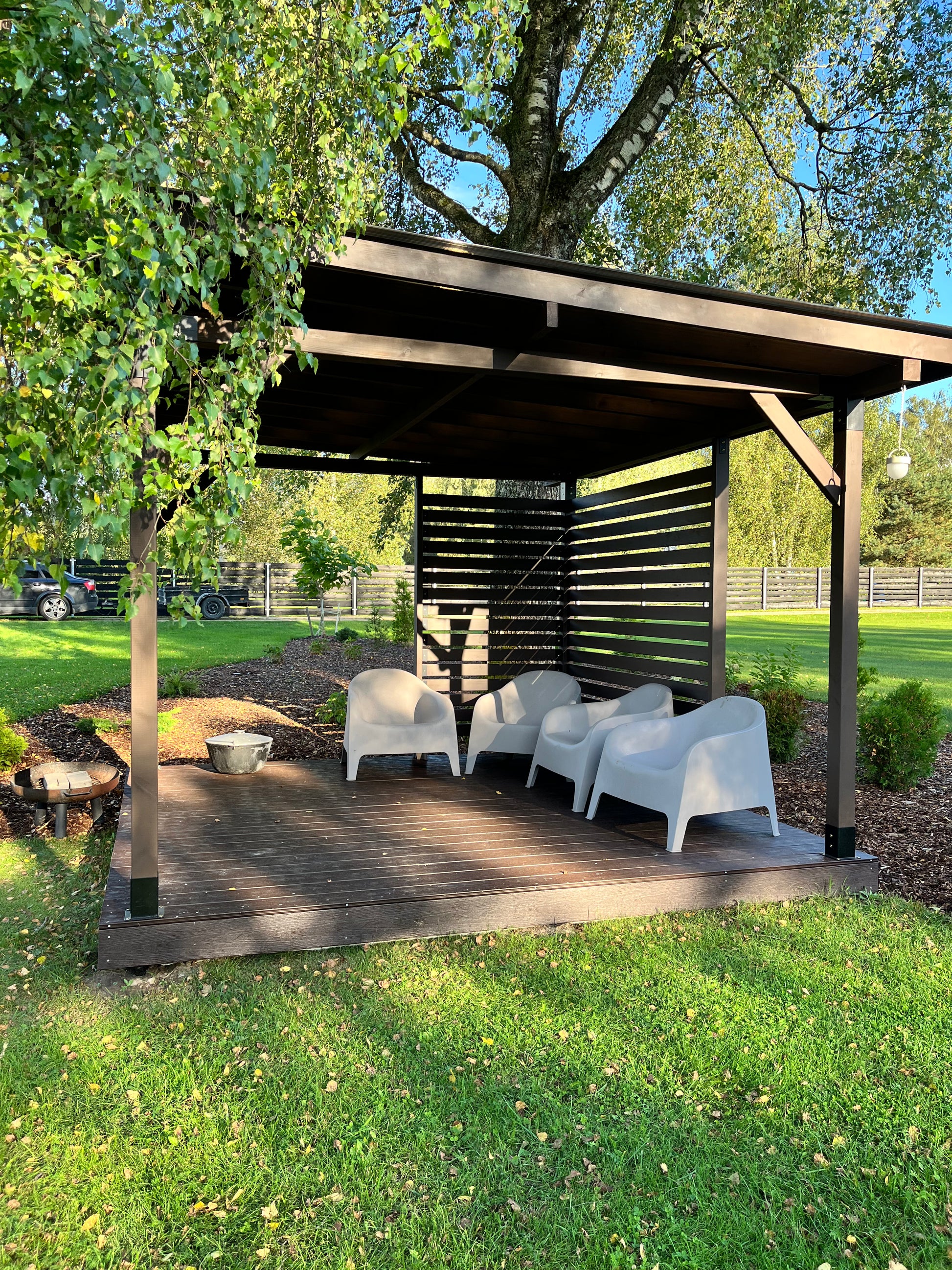 Outdoor wooden gazebo with white chairs on a grassy area