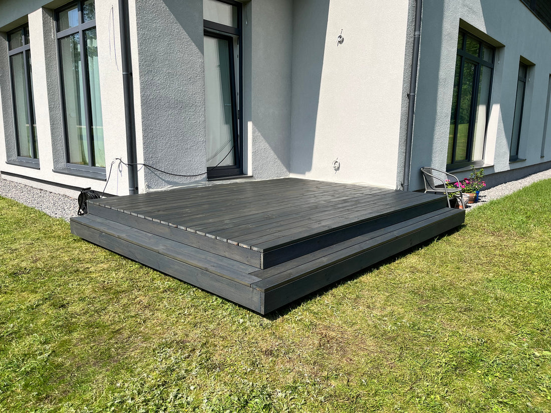 Wooden deck in front of a modern house with grass and a building in the background