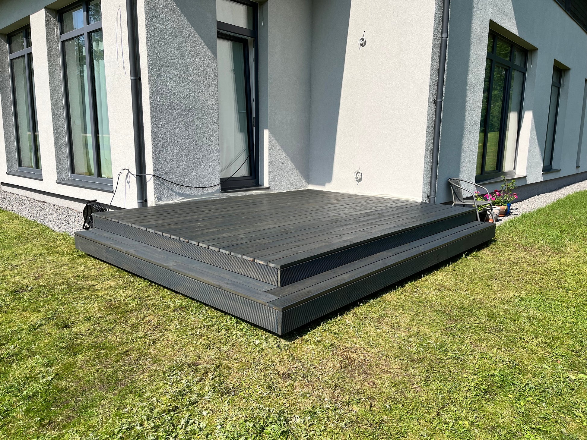 Wooden deck in front of a modern house with grass and a building in the background