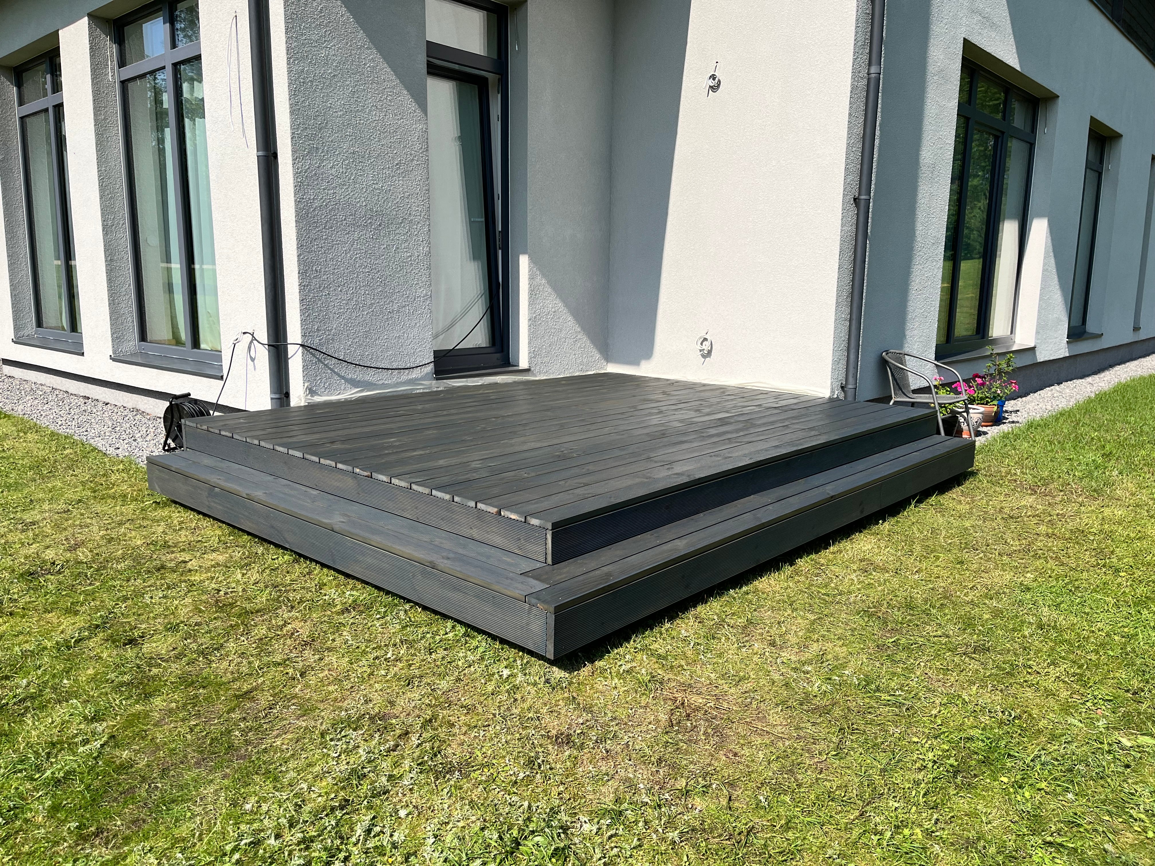 Wooden deck in front of a modern house with grass and a building in the background
