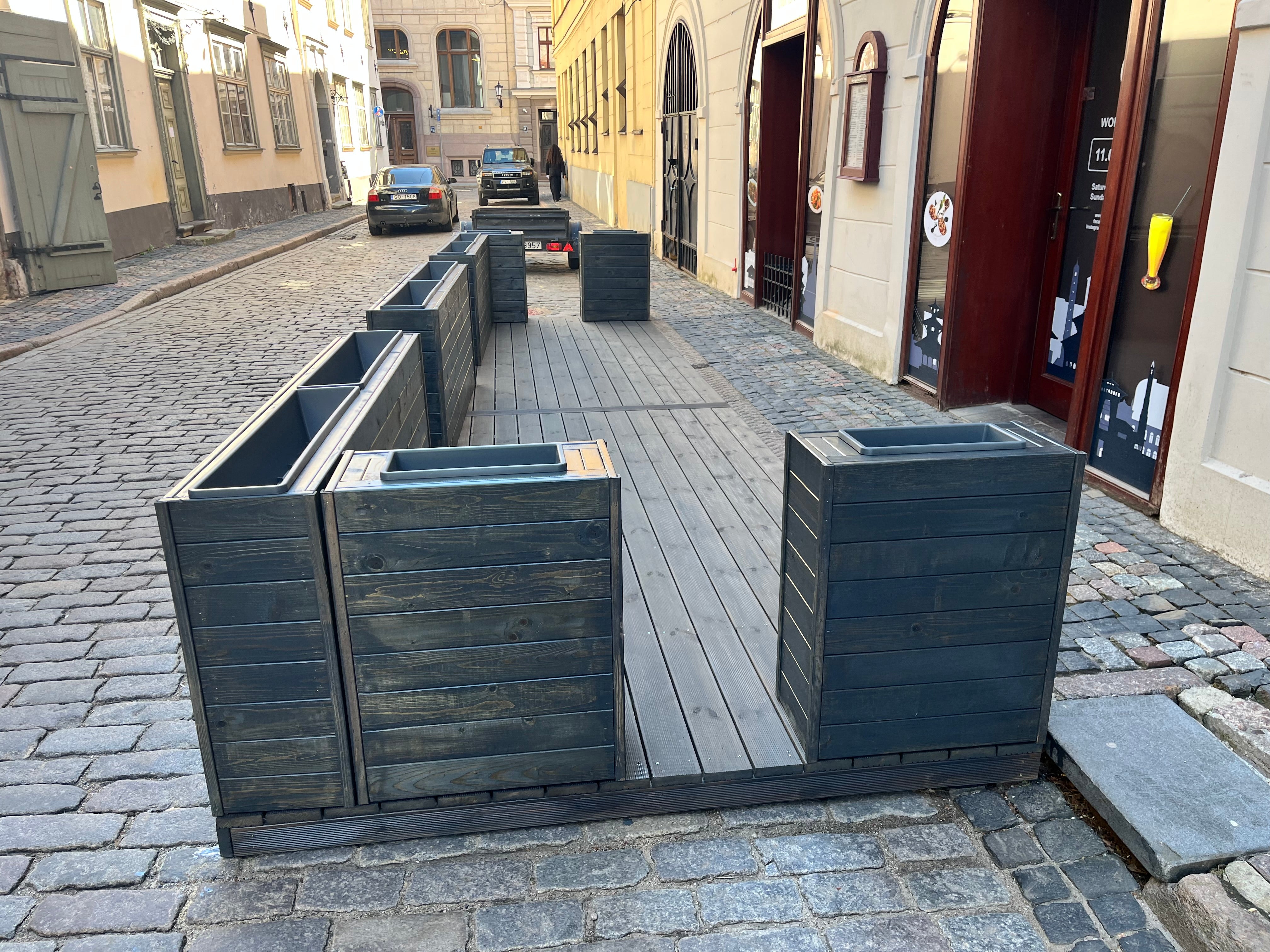 Stacked black metal planters on a cobblestone street with buildings in the background