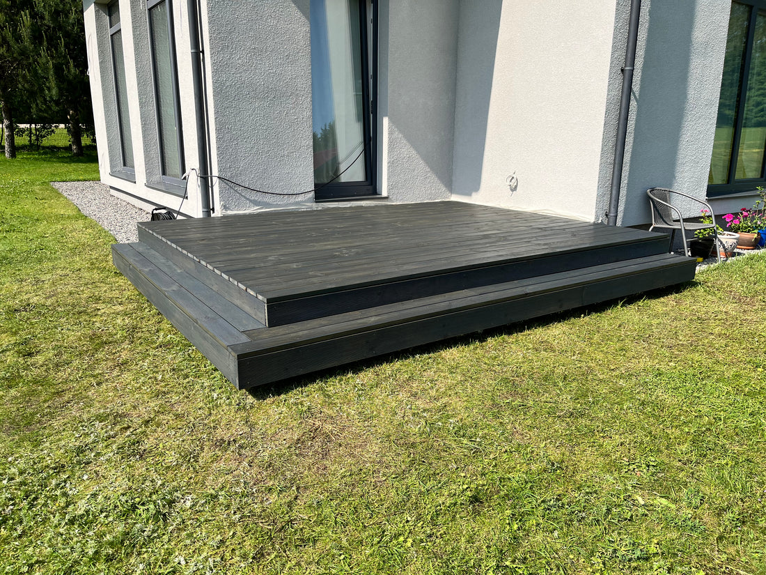 Wooden deck in front of a modern house with grass and a building in the background