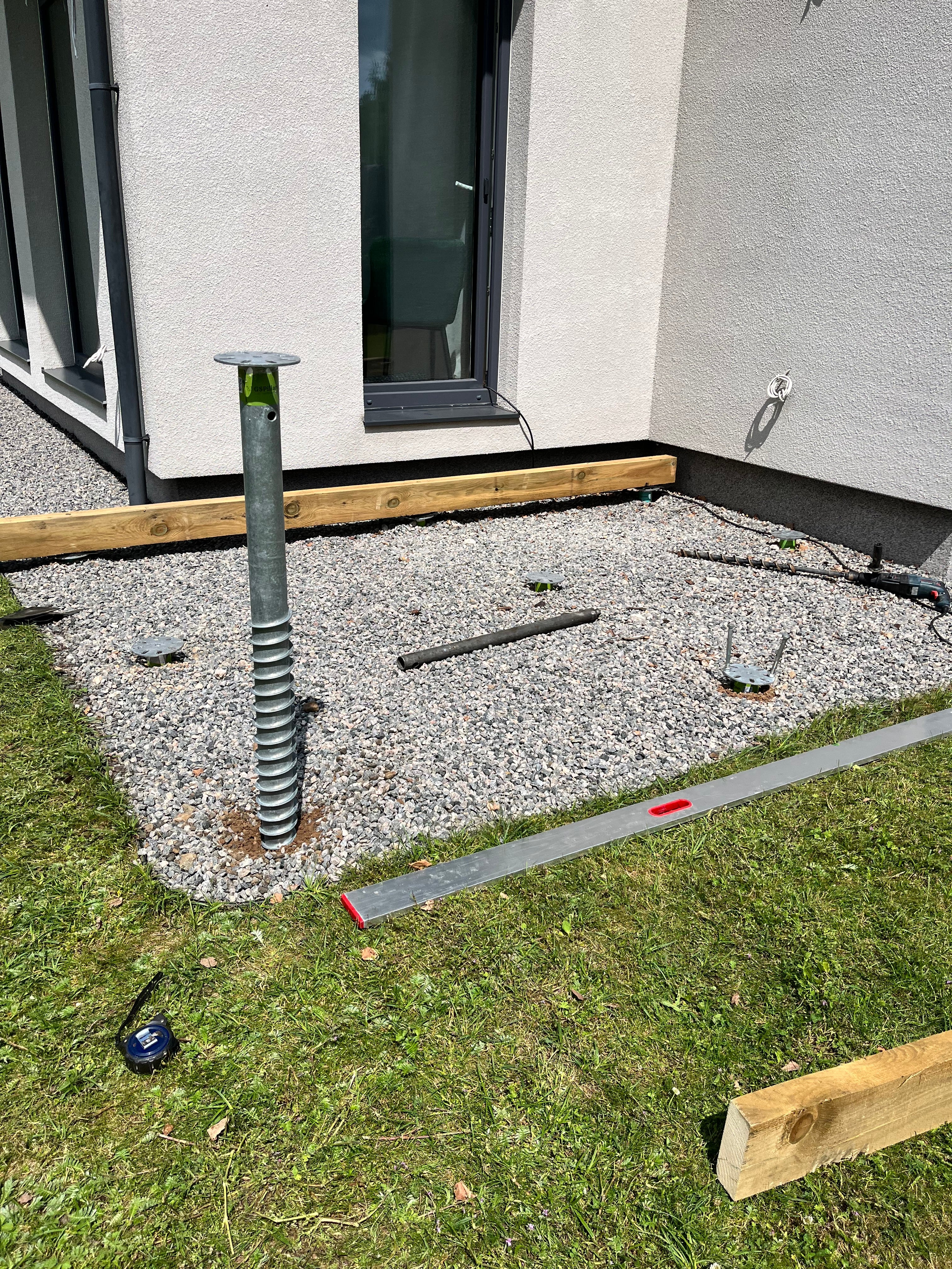 Construction site with gravel, metal rods, and a house in the background