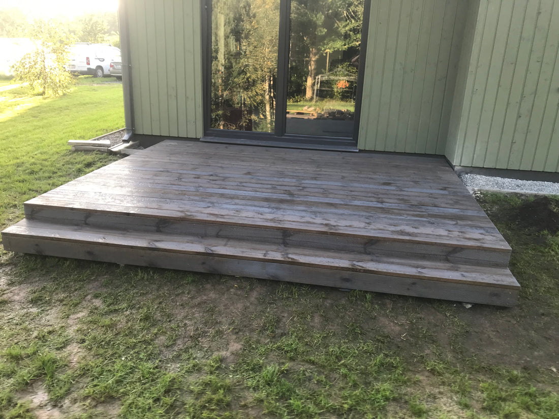 Wooden deck with steps leading up to a house with large windows.