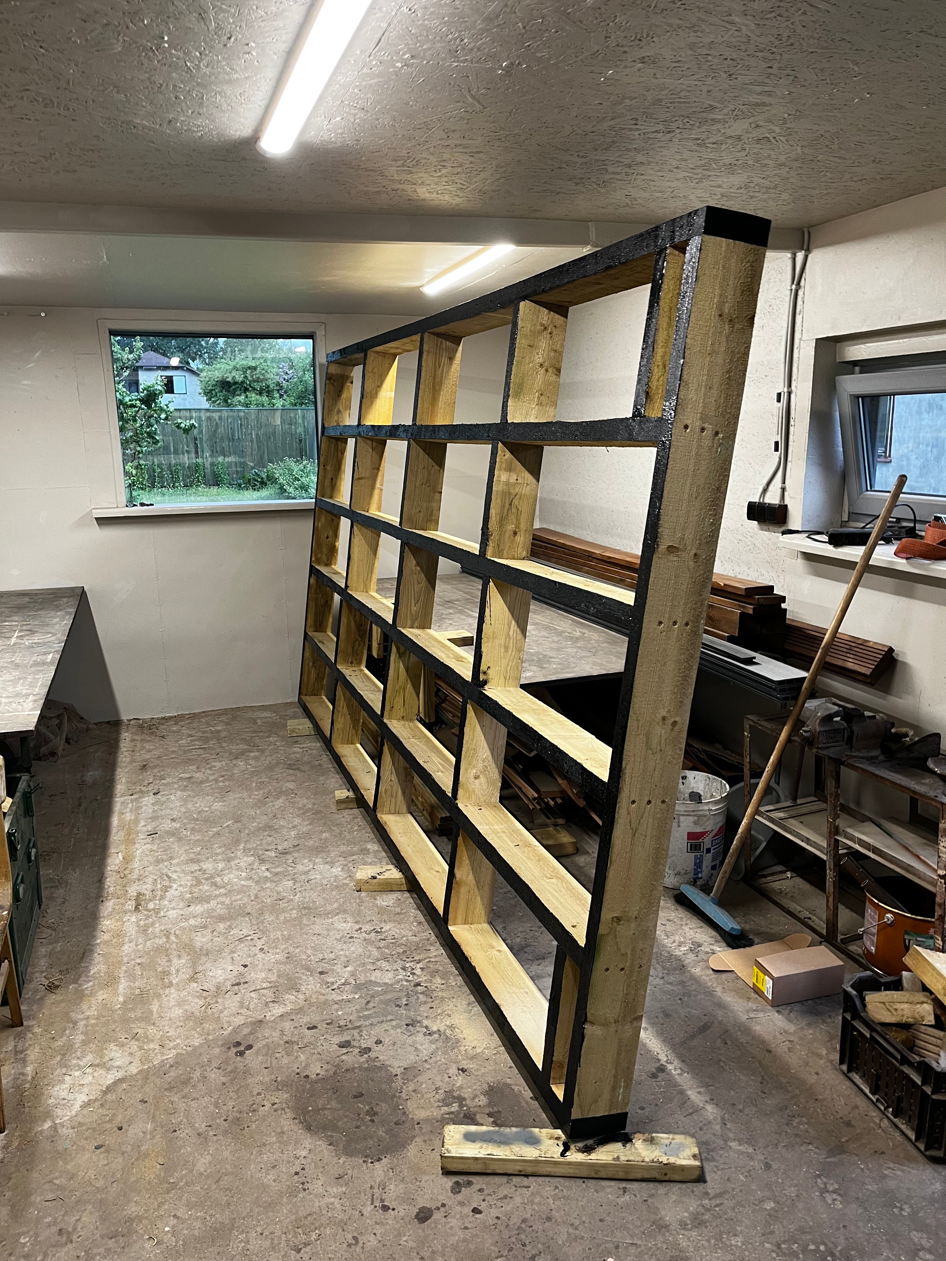 Wooden deck frame structure against a concrete wall with a window in the background