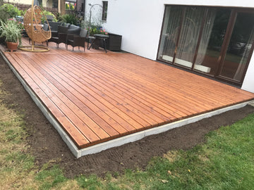 Wooden deck being built in a backyard with outdoor furniture.