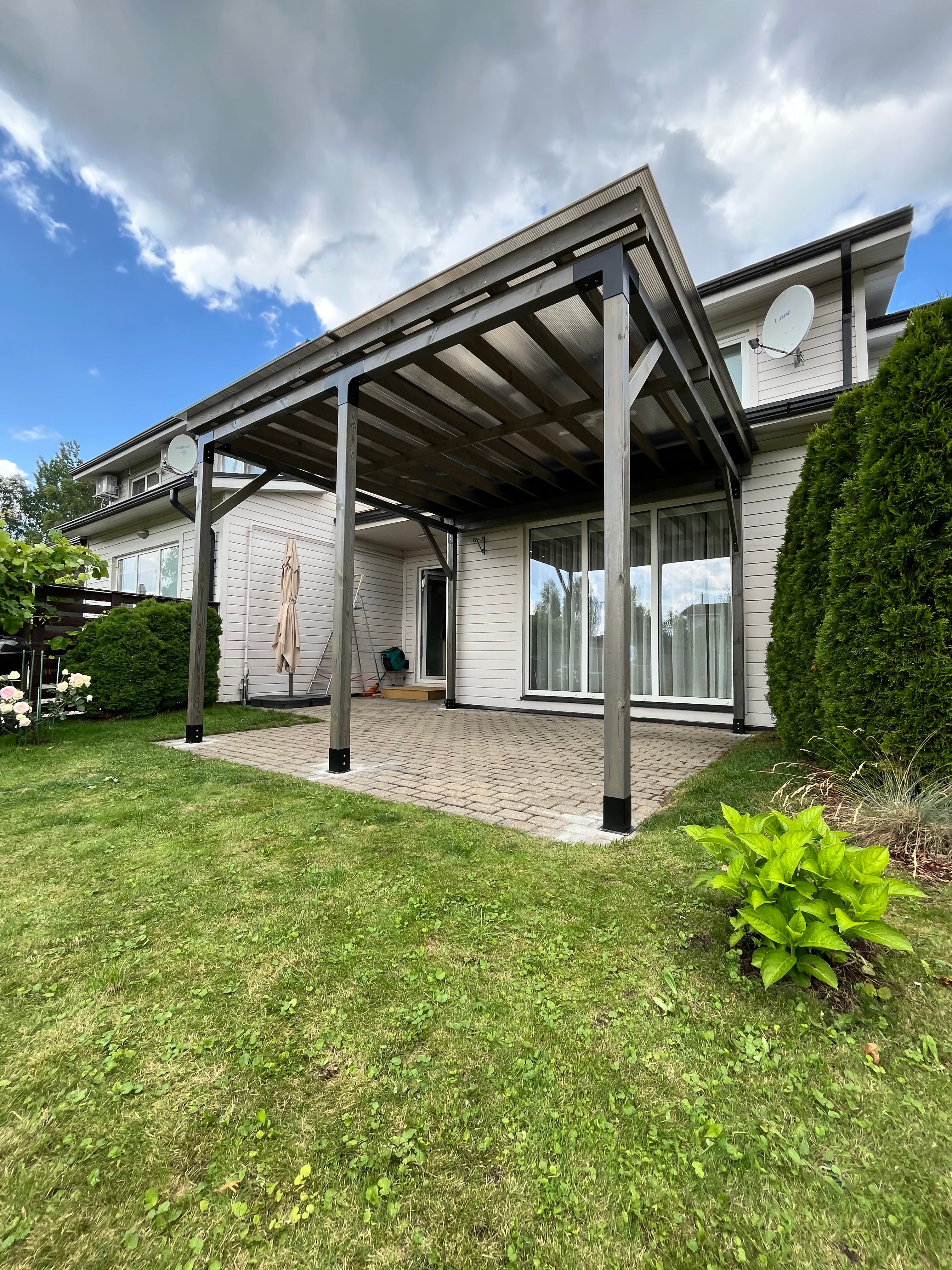 Patio with glass walls on a sunny day, surrounded by greenery.