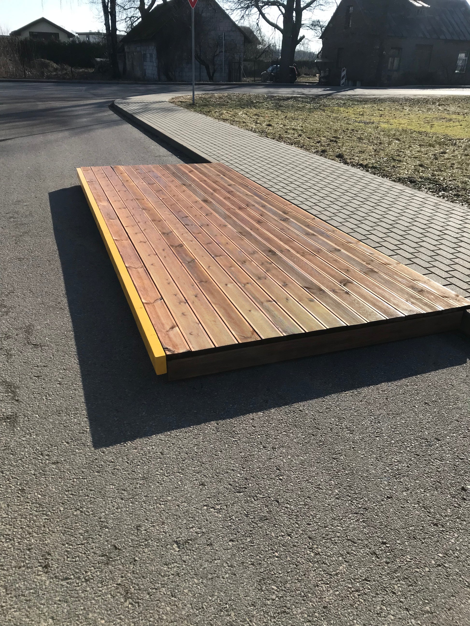 Wooden deck or platform on a street corner with grass and pavement in the background