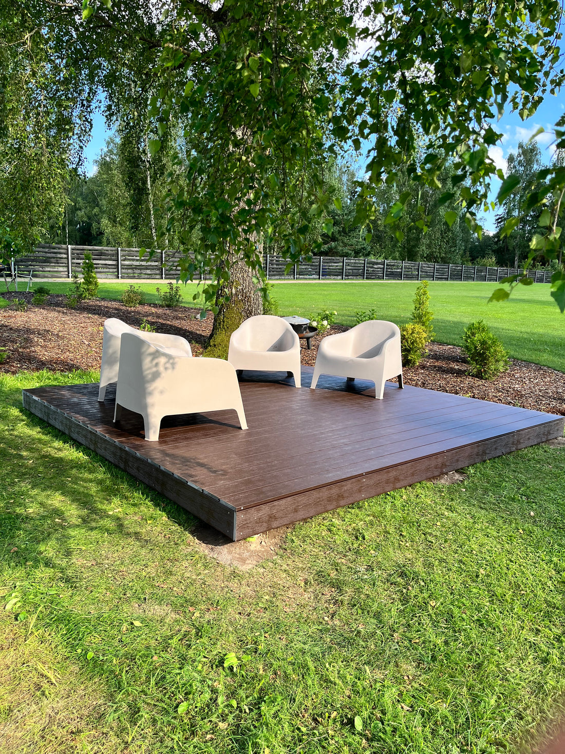 Wooden outdoor deck with chairs on a grassy area with trees in the background