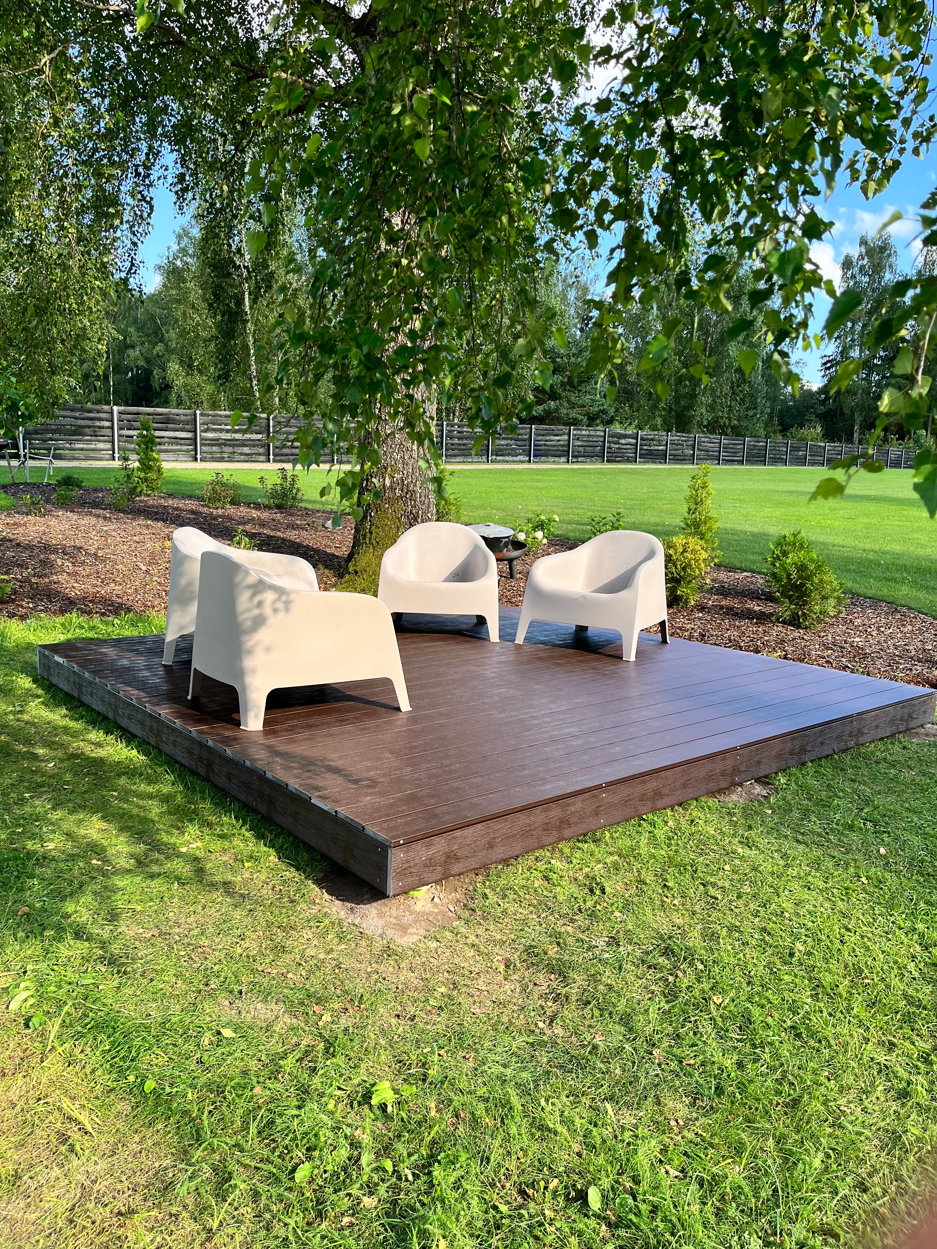 Wooden outdoor deck with chairs on a grassy area with trees in the background